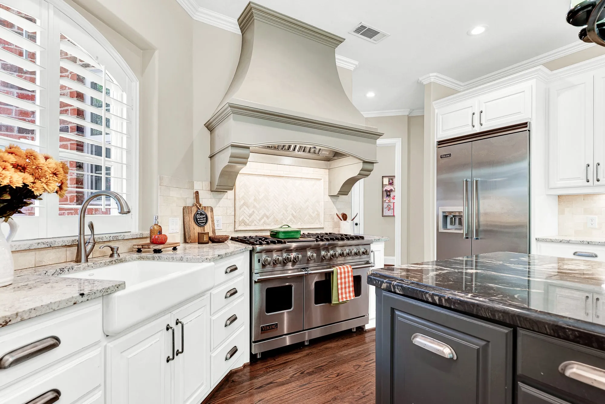 A sculpted hearth-style range hood anchors the cooking alcove, catching bright light from an arched window. Visualize simmering a savory dinner sauce on a cozy weeknight.