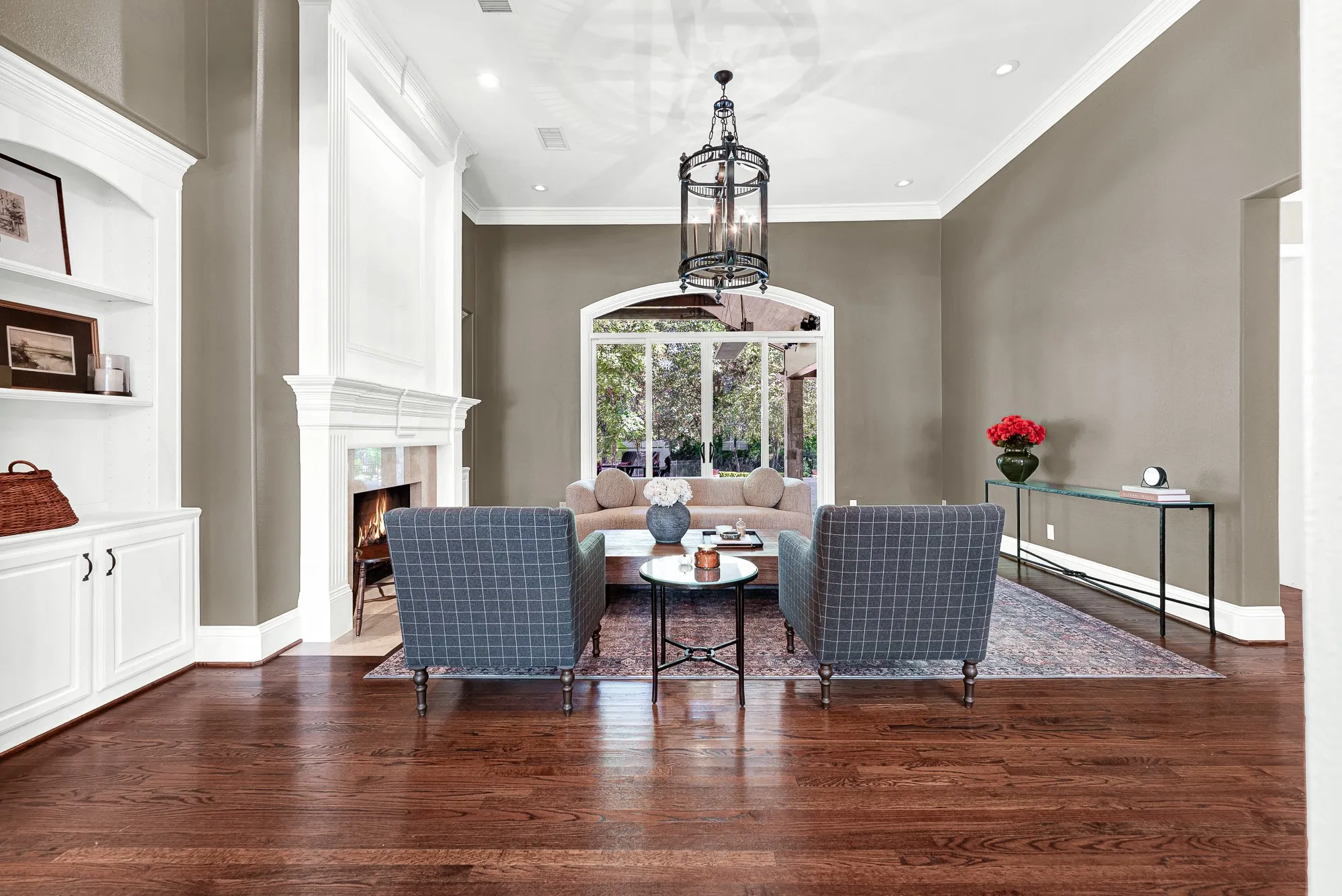 An grand floor-to-ceiling hearth mantle centers the room, framing bright outdoor light filtered through an arched patio wall. Picture yourself unwinding by a roaring fire while soft afternoon sun settles across the warm hardwood floors.