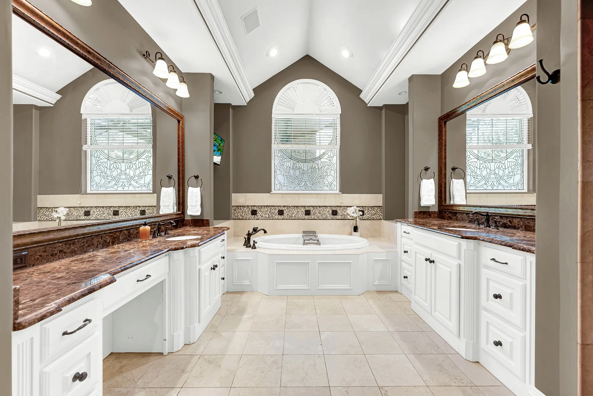 A dramatic vaulted ceiling directs sunlight straight toward an arched, leaded-glass window over the drop-in tub. Indulge in a long, luxurious bath surrounded by soft, ambient light.