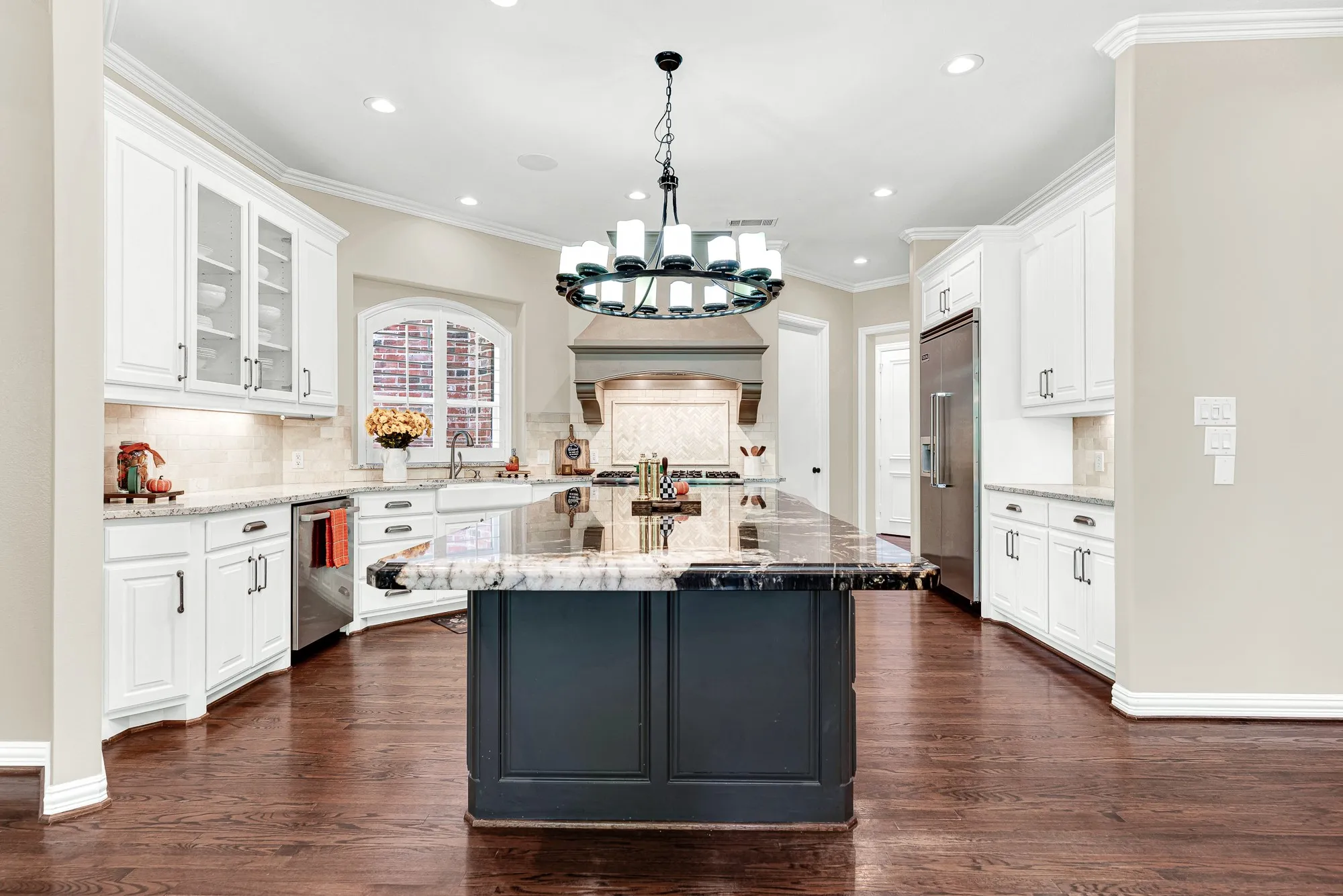 An expansive central island grounds the open kitchen beneath warm, balanced overhead lighting. Picture prepping weekend brunch while family gathers around to chat.