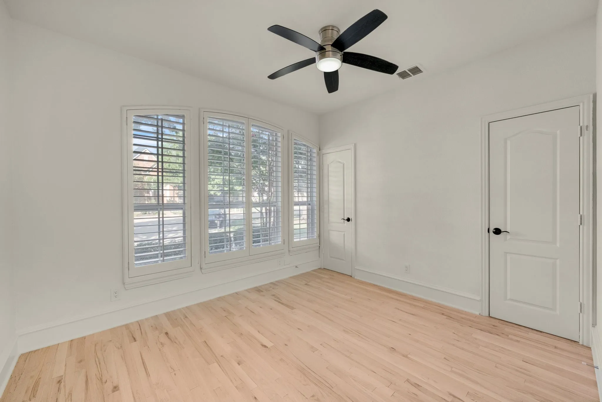 Hardwood flooring, plantation shutters, contemporary ceiling fan, arched windows, and paneled doors