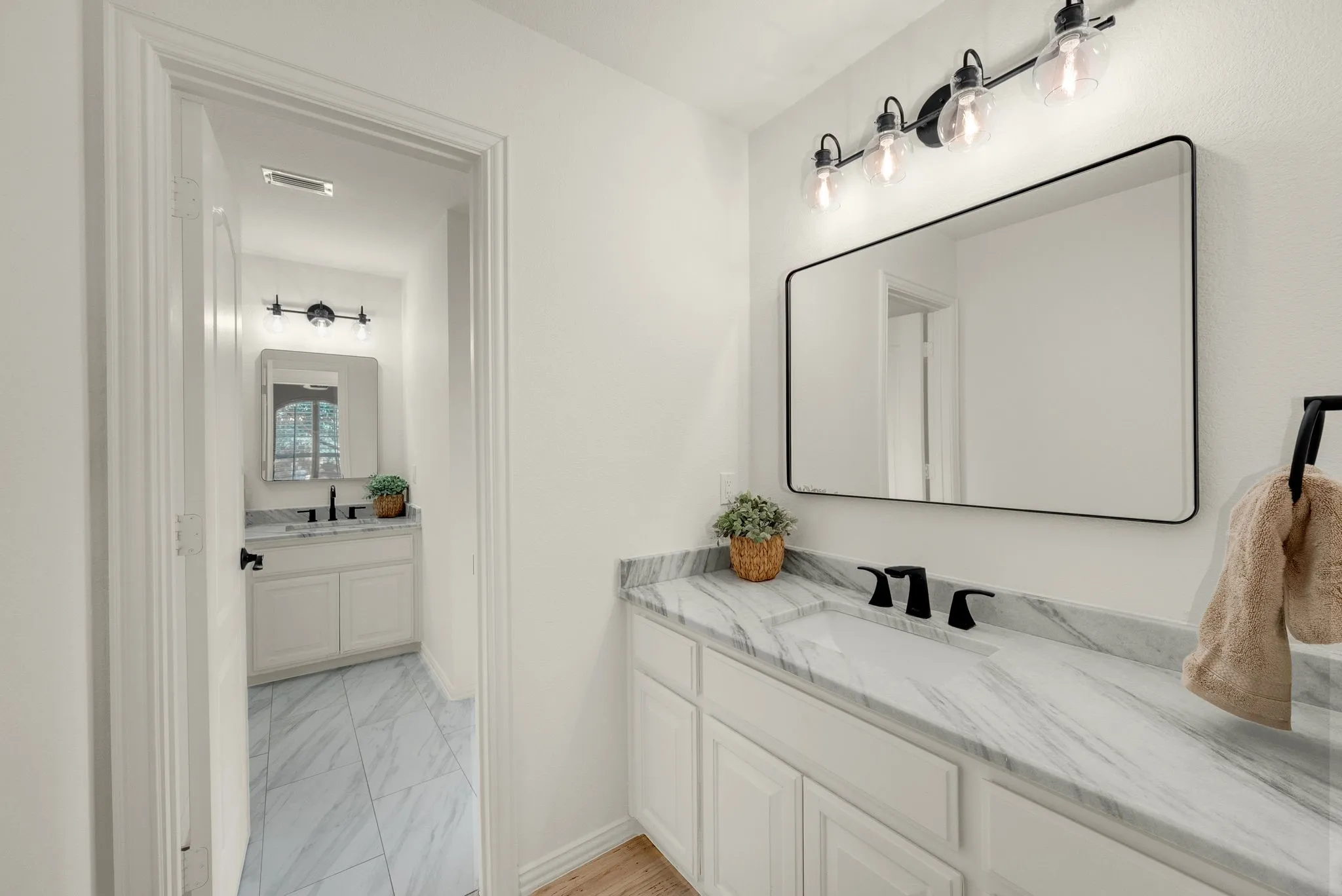 White vanity with a stone countertop, featuring a rectangular undermount sink and matte black faucet