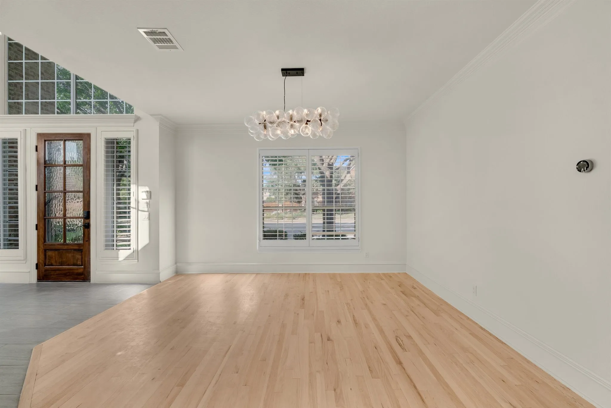 Hardwood flooring, modern chandelier, crown molding, plantation shutters, and a decorative glass paneled entry door