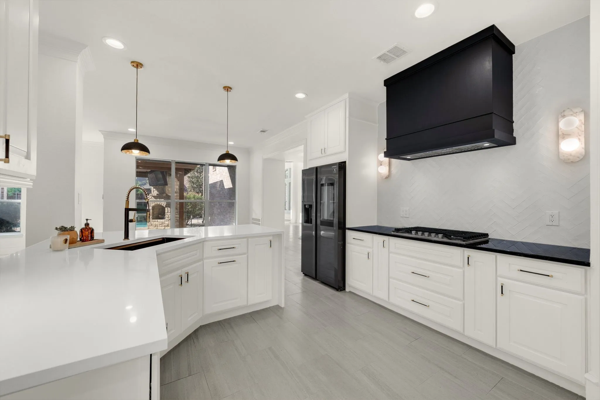 Modern kitchen featuring white cabinetry with brushed metal hardware, white quartz countertops, stainless steel appliances including a gas cooktop, pendant lighting with bronze fixtures, and gray wood-finish flooring throughout the open layout