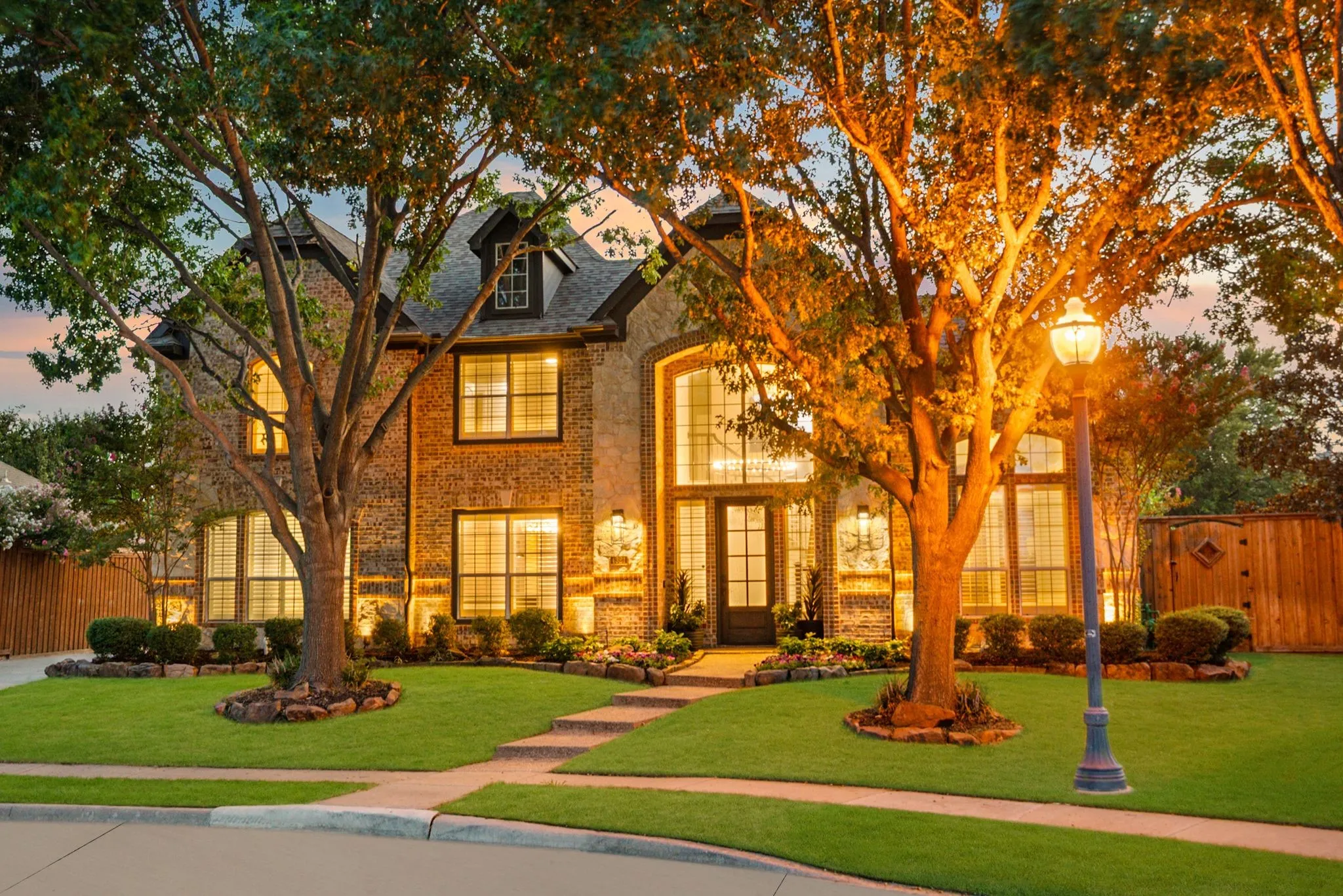 Brick and stone facade with multiple window styles, mature trees, and a manicured lawn