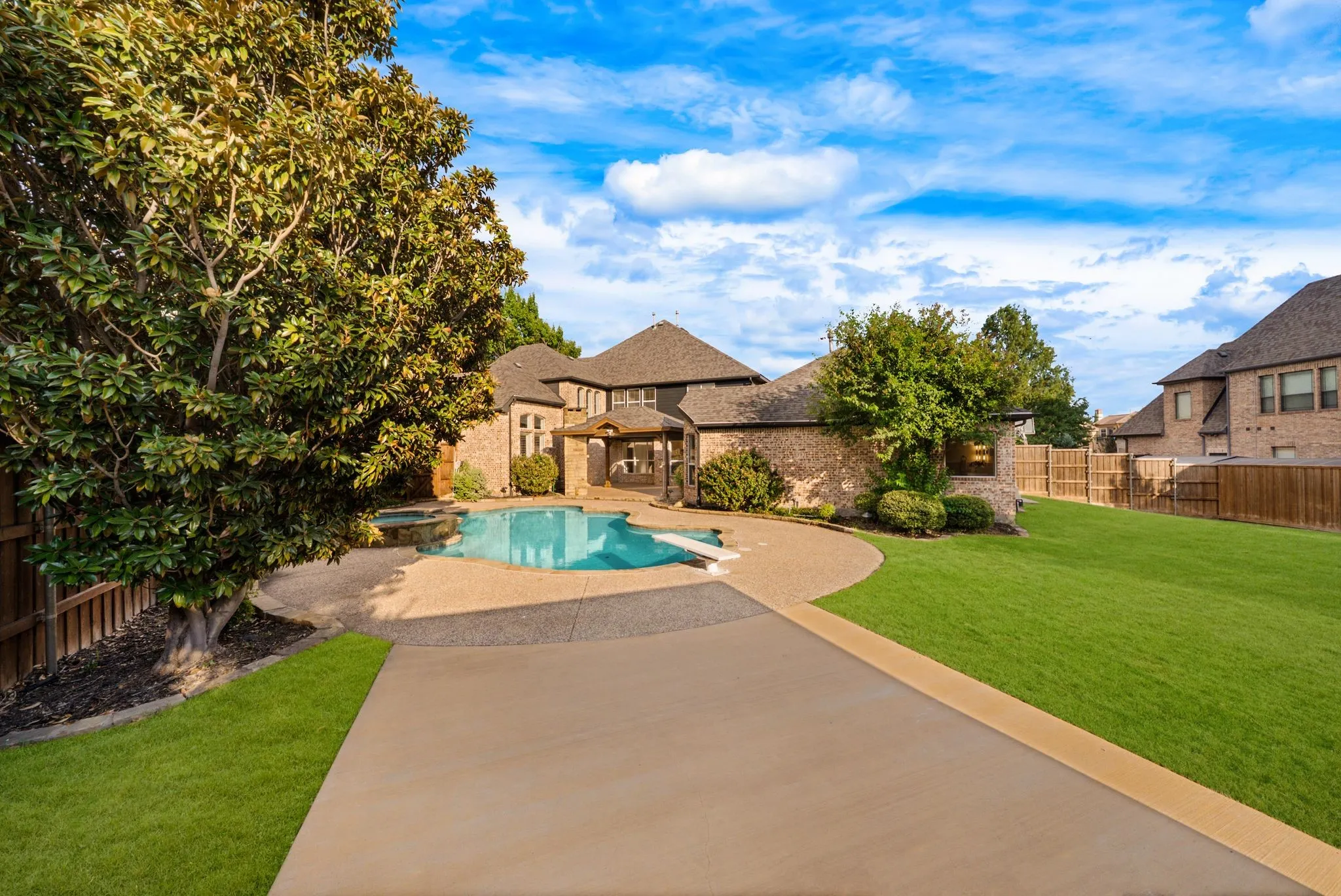 Expansive backyard oasis featuring a resort-style swimming pool with integrated spa, mature landscaping including specimen trees, manicured lawn, concrete hardscaping, and stone architectural elements