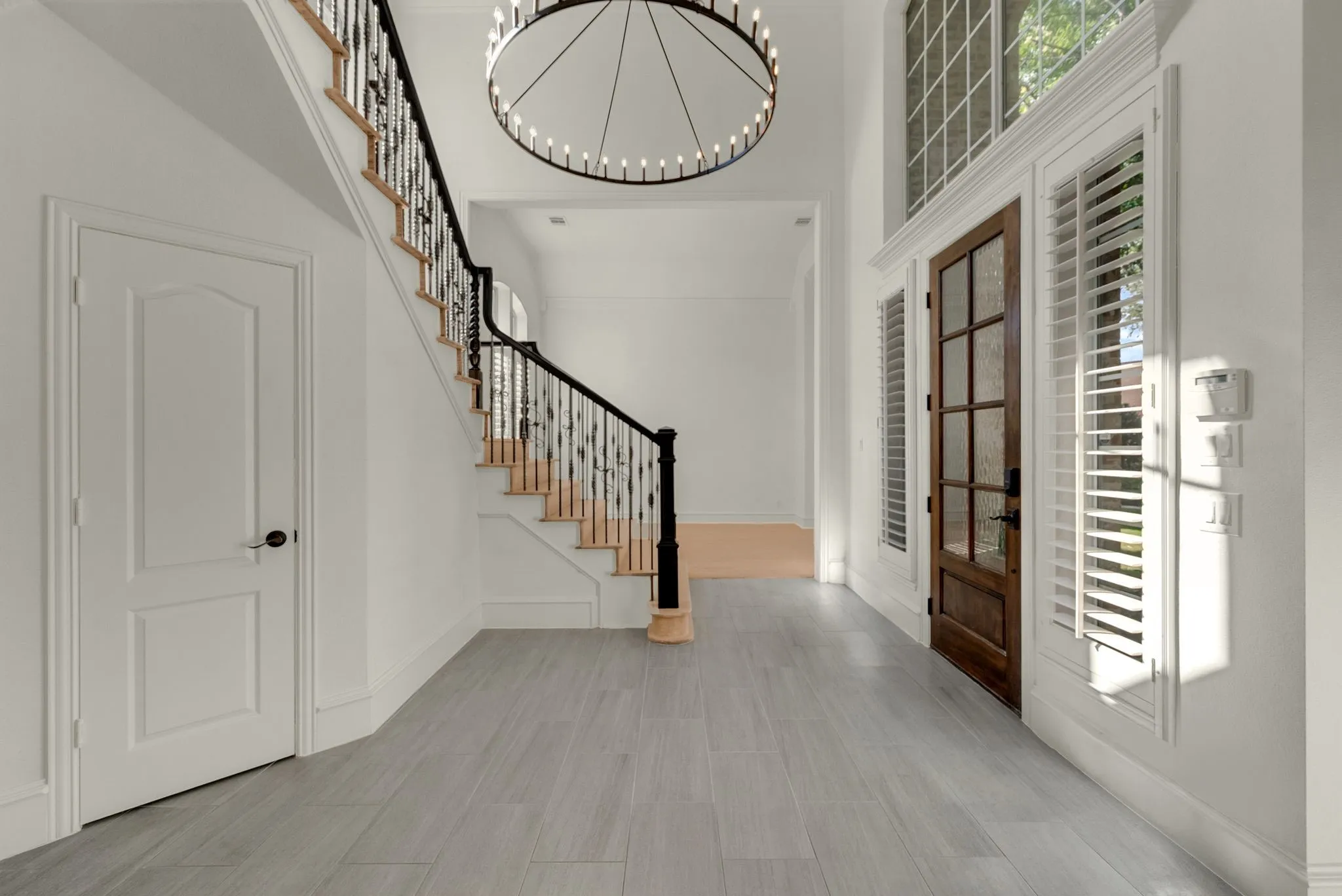 Bright foyer showcasing soaring ceilings, a curved staircase with black metal railings and wood treads, wide-plank wood-finish flooring, and a geometric pendant light fixture