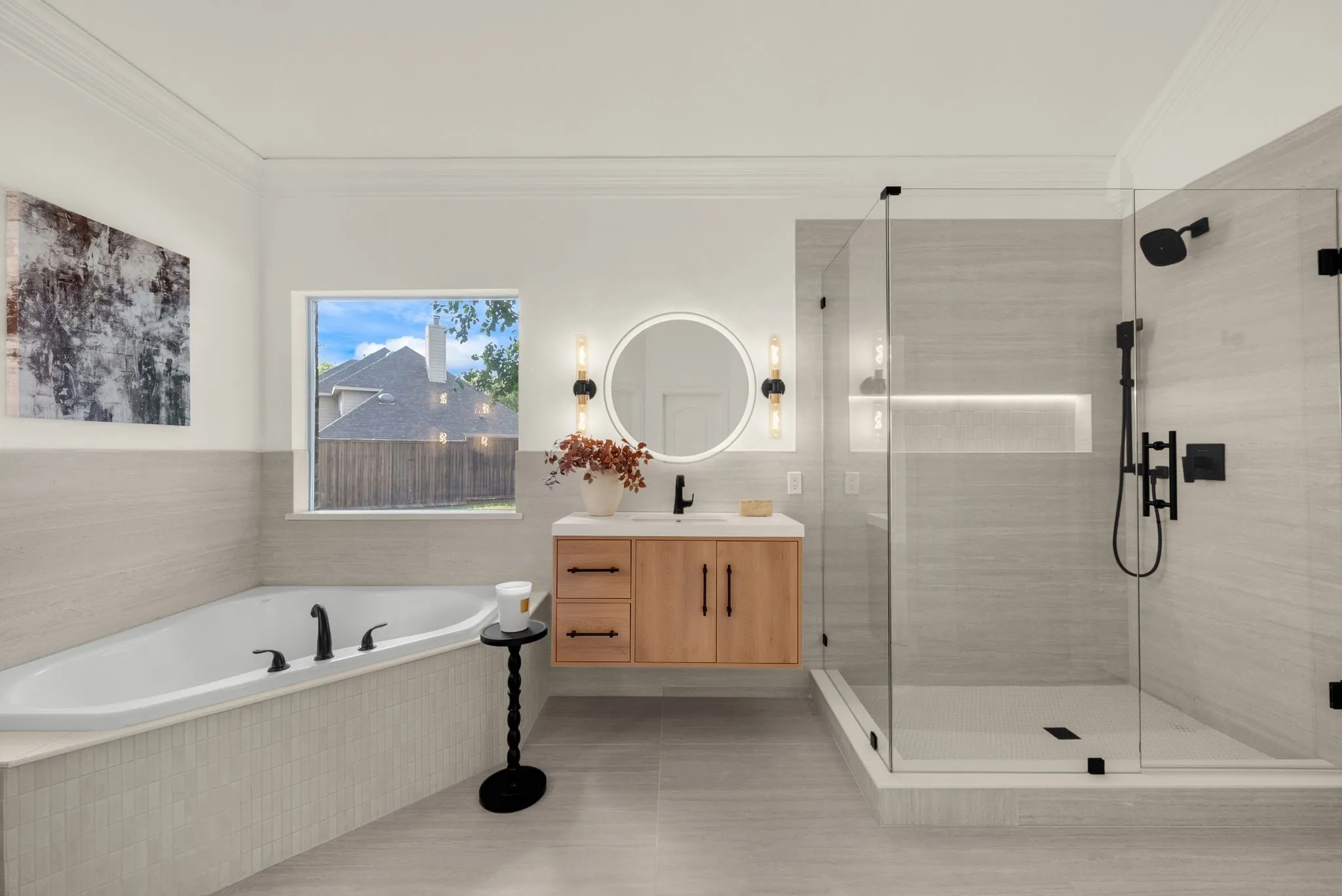 Spacious bathroom featuring a built-in soaking tub, a floating wood-finish vanity with a vessel sink, a walk-in glass-enclosed shower with matte black fixtures, a round backlit mirror, and sconce lighting