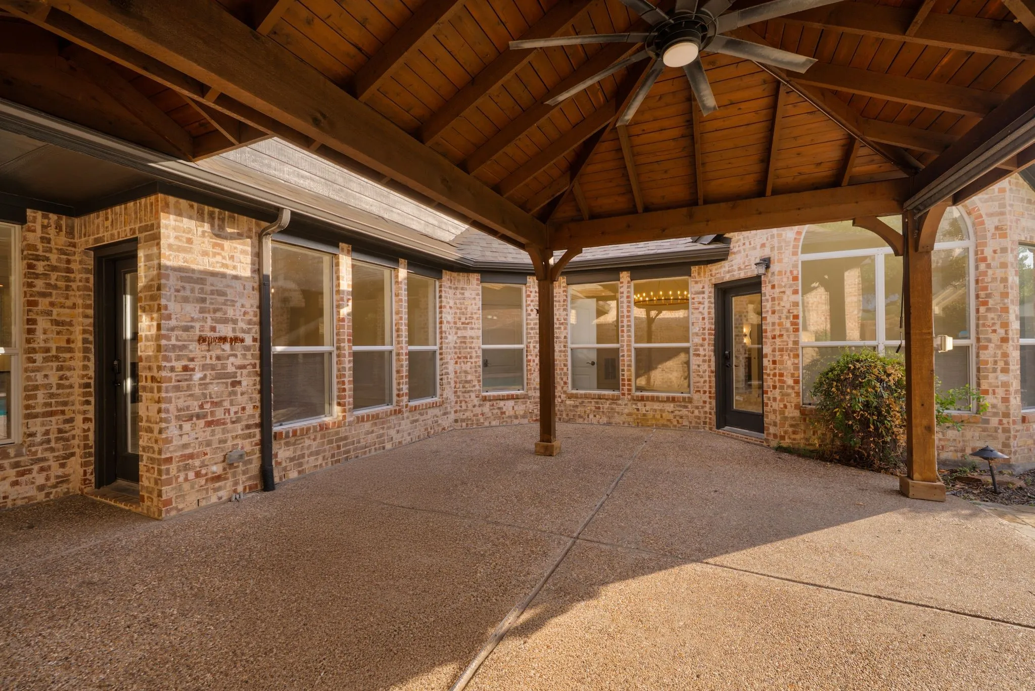 Expansive covered patio featuring an exposed aggregate concrete surface, wood-finish vaulted ceiling, and an integrated ceiling fan