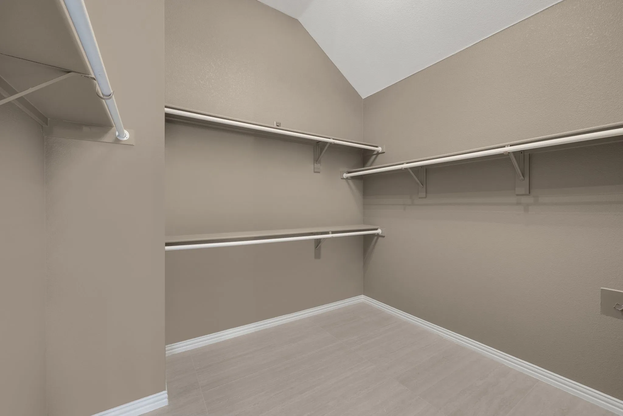 Spacious walk-in closet featuring multiple chrome-finished hanging rods, white wood-finish flooring, and soft recessed lighting throughout