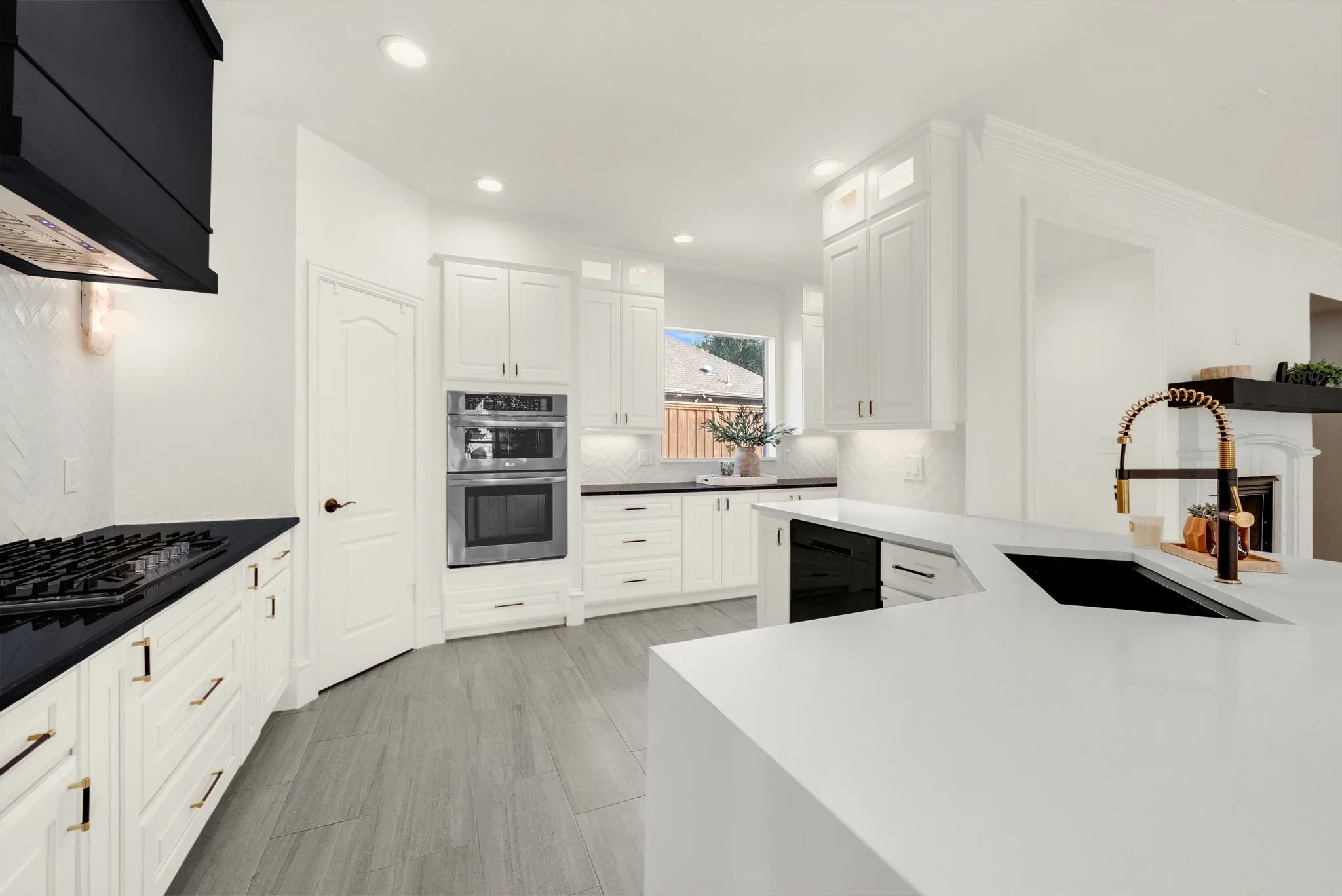 White shaker cabinetry with gold-tone hardware, black countertop surfaces, stainless steel double wall oven, gas cooktop with black range hood, and tile flooring
