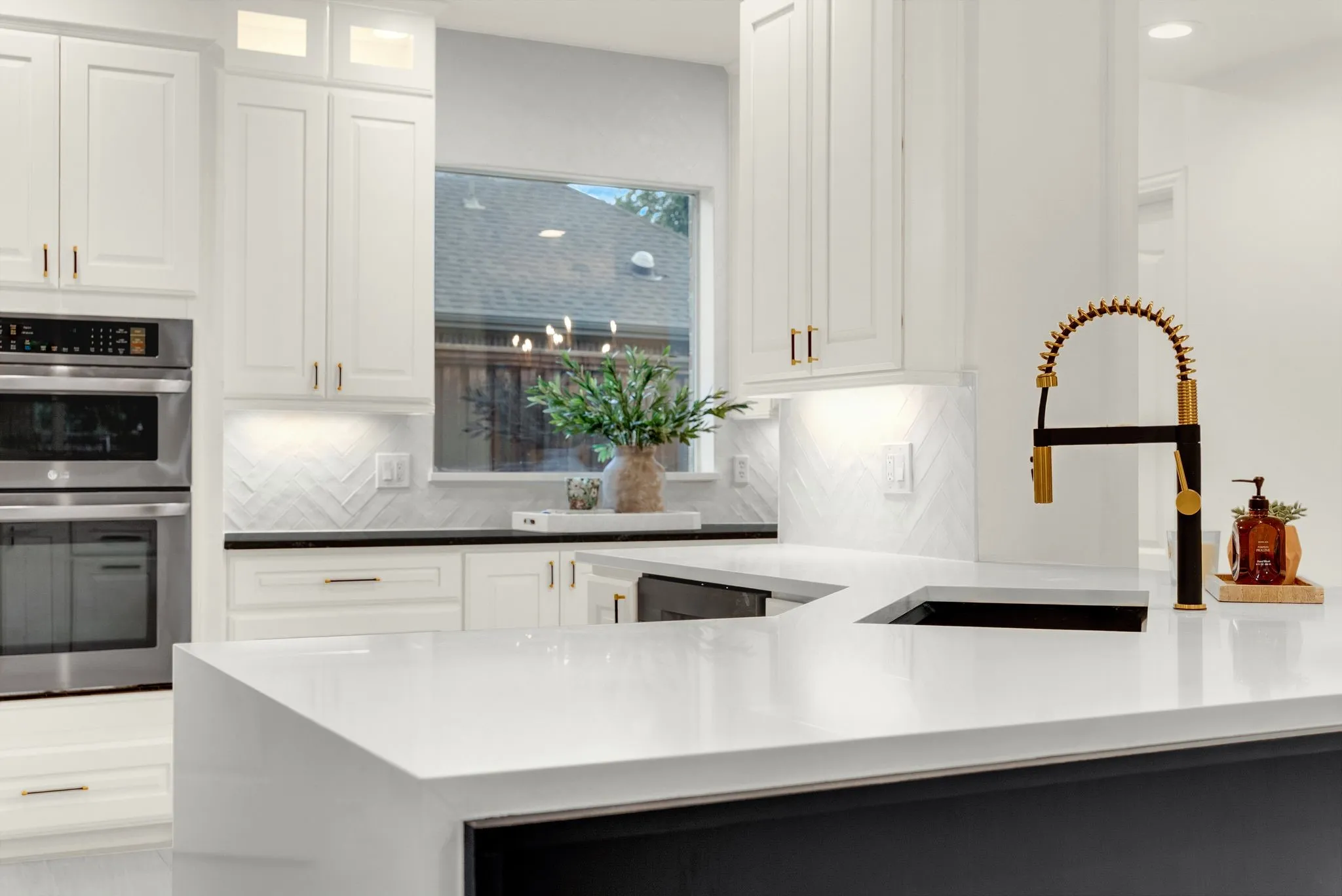 Gourmet kitchen featuring white shaker cabinetry, stainless steel double ovens, a white herringbone tile backsplash, and a black and gold gooseneck faucet