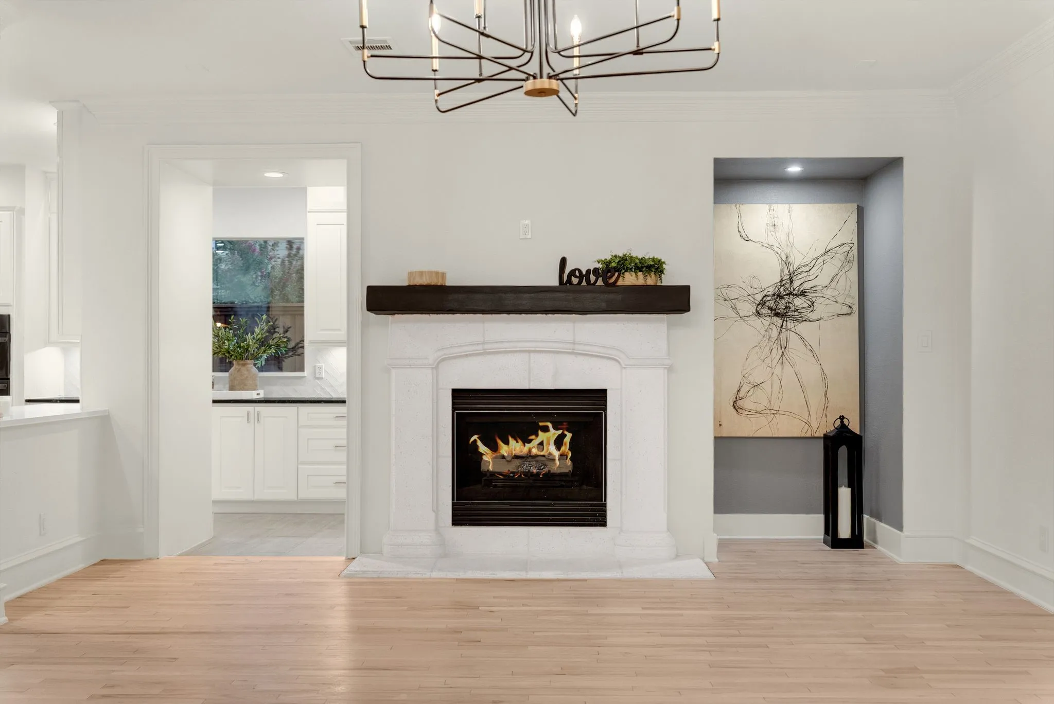 Hardwood flooring extending throughout, a fireplace with a white stone surround and dark wood-finish mantel, and a recessed art niche with integrated lighting