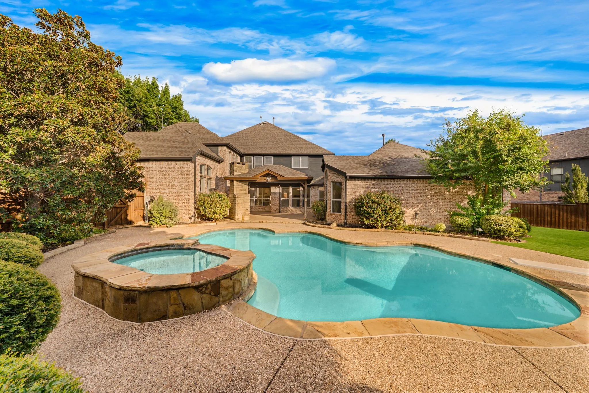 Brick exterior with multiple gables, a large pool, a raised spa with stone veneer, and mature landscaping