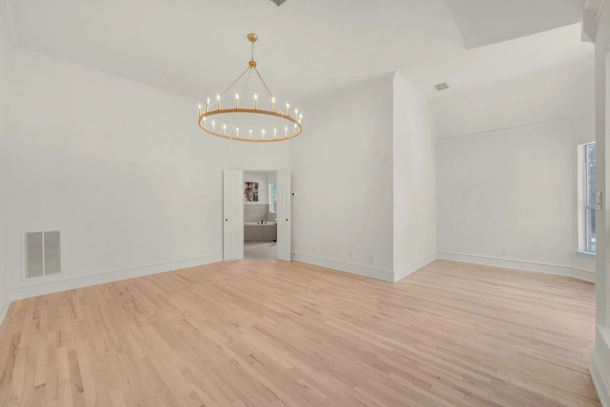 Expansive room with natural wood flooring and a large circular chandelier