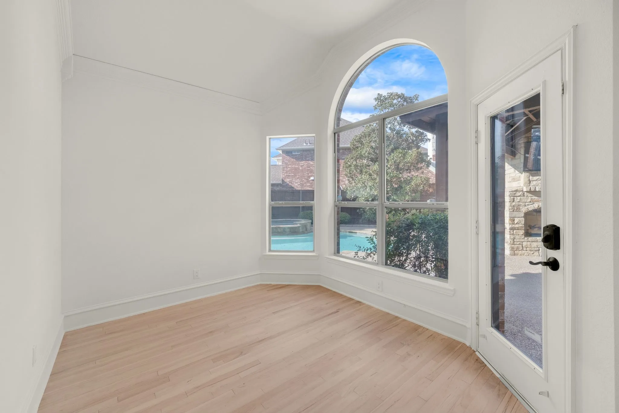 Room featuring light wood-finish flooring, white walls, and a large arched window