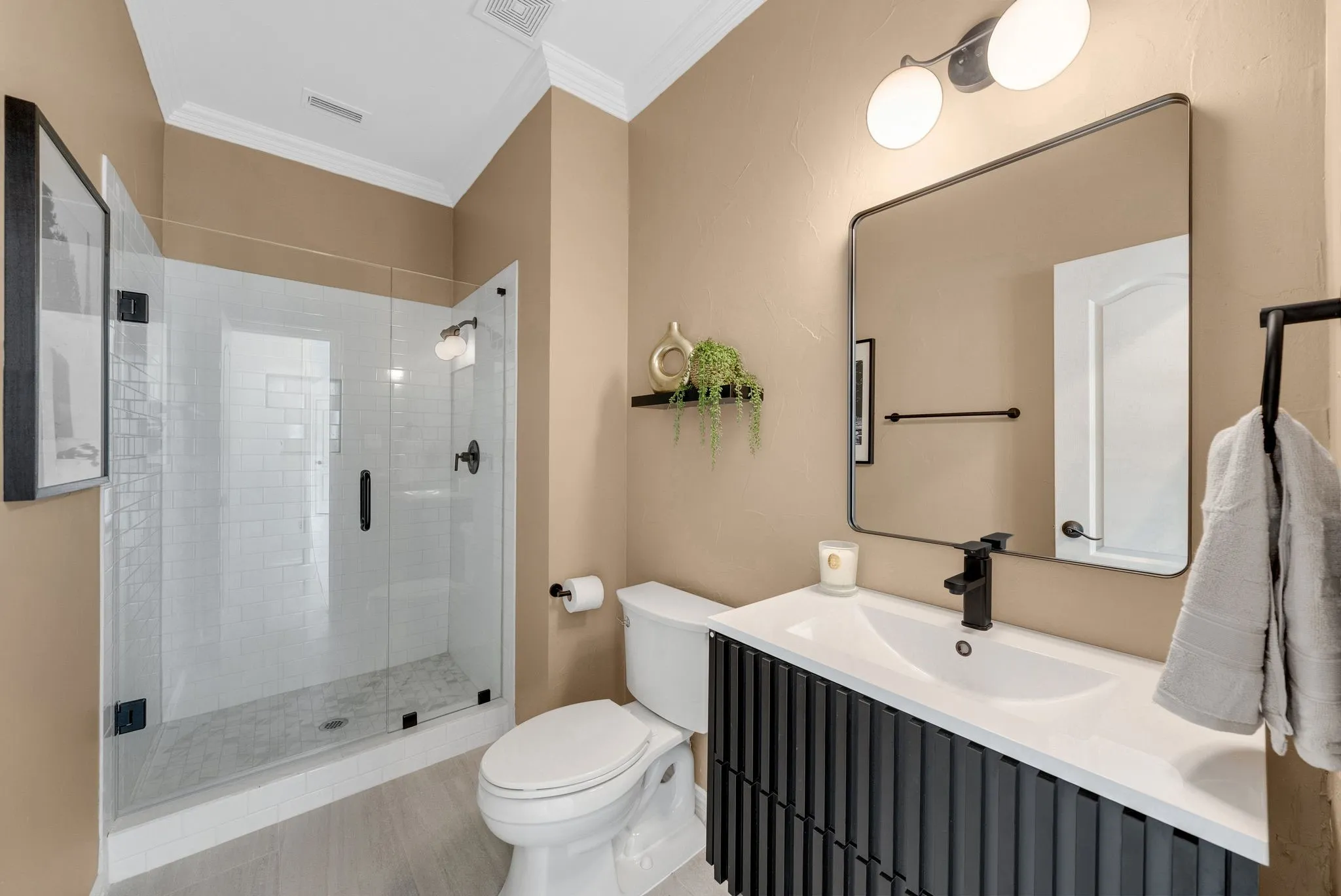 Glass-enclosed shower with subway tile, built-in vanity with integrated sink, black hardware, wall-mounted light fixture, and large framed mirror