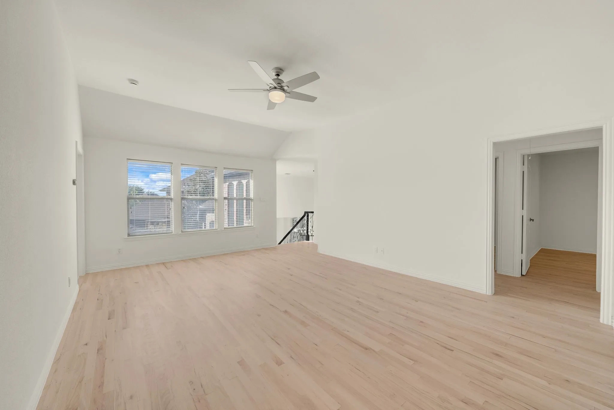 Vaulted ceiling, ceiling fan, wood-finish flooring, three large windows, and white walls