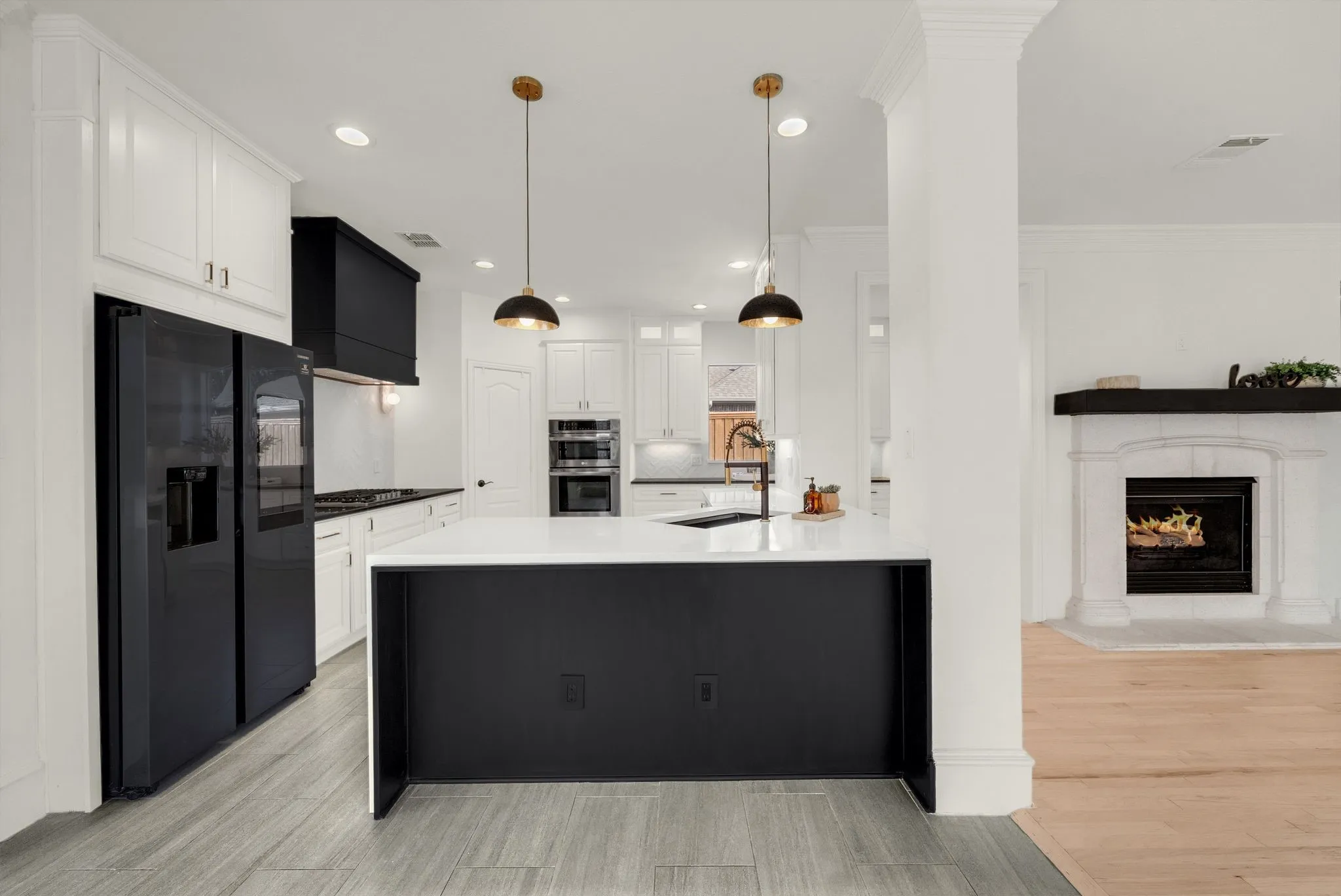 Open concept kitchen with a large central island, white cabinetry, integrated stainless steel appliances, and two pendant light fixtures