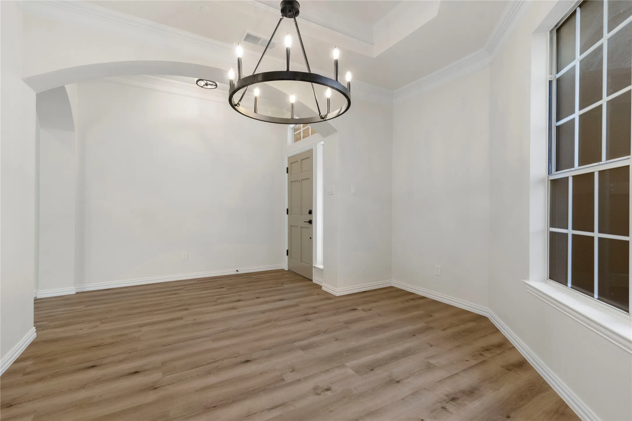 Wood-finish flooring, white walls, arched entryway, tray ceiling, and a prominent window with grid-patterned panes