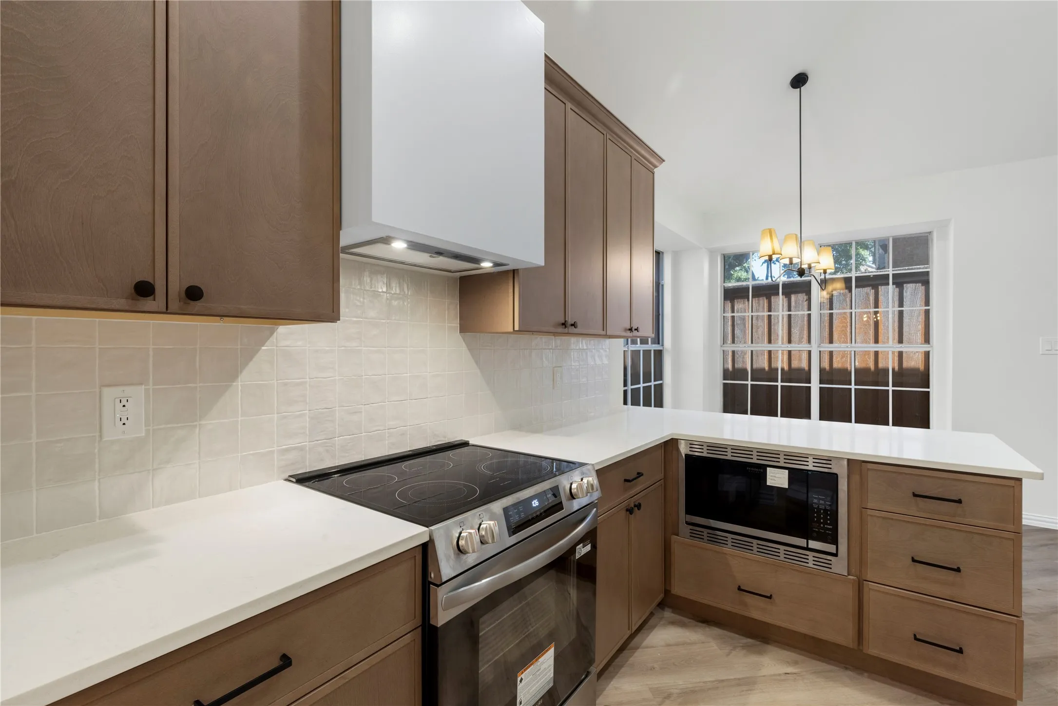Kitchen featuring wood-finish cabinetry, white countertops, a mosaic tile backsplash, stainless steel oven with cooktop, and an integrated microwave