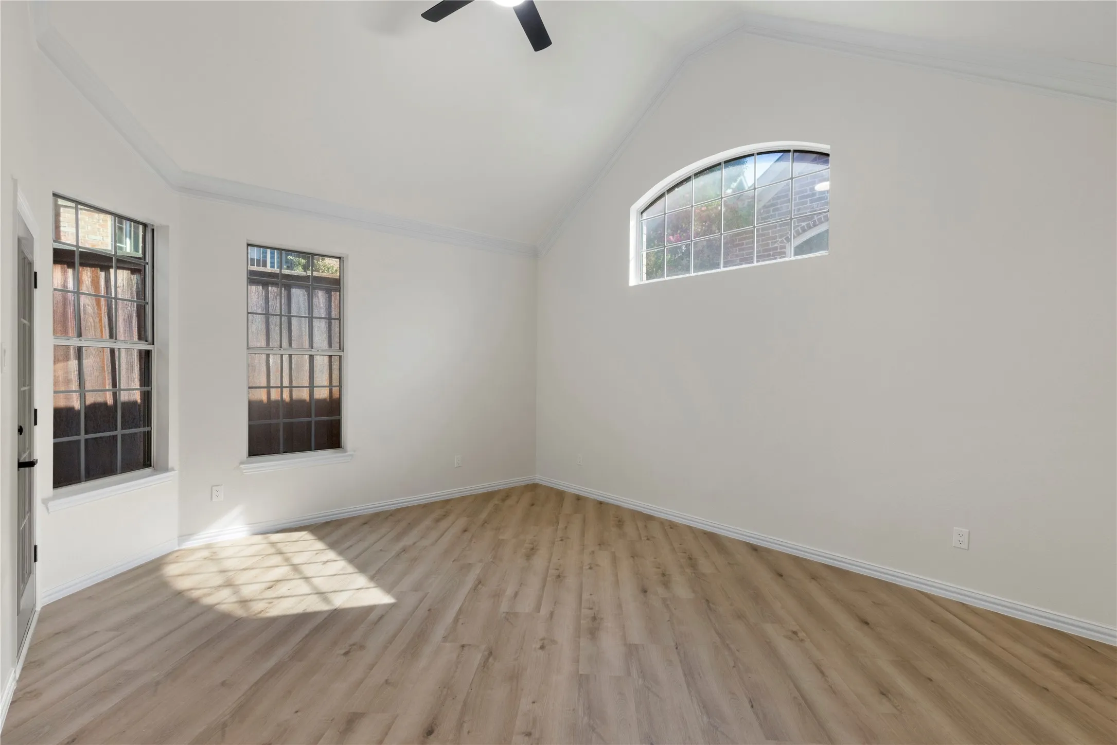 Vaulted ceiling with crown molding, wood-finish flooring, and arched window