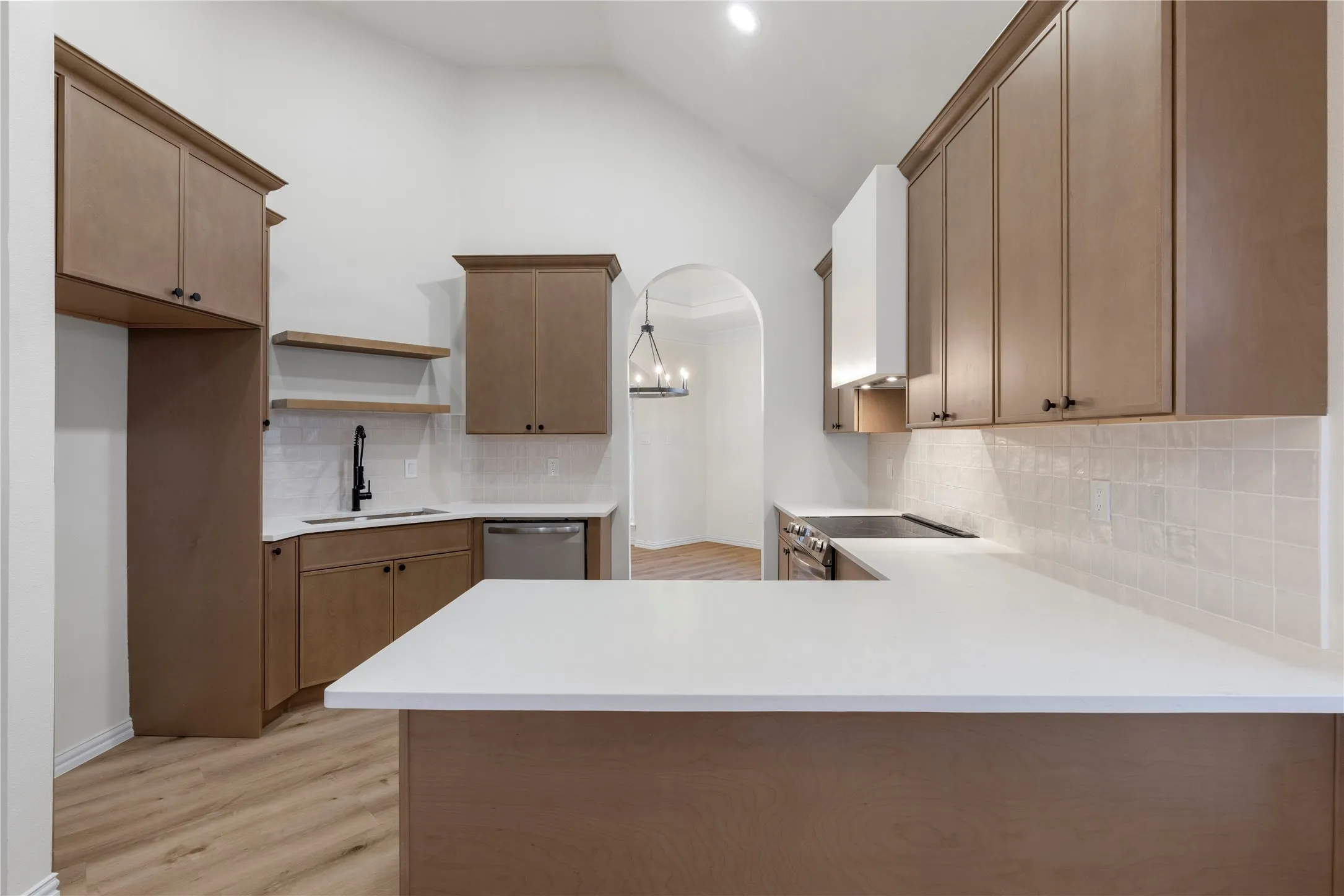 Vaulted ceiling, wood-finish flooring, white countertops, built-in cabinetry, and a subway tile backsplash