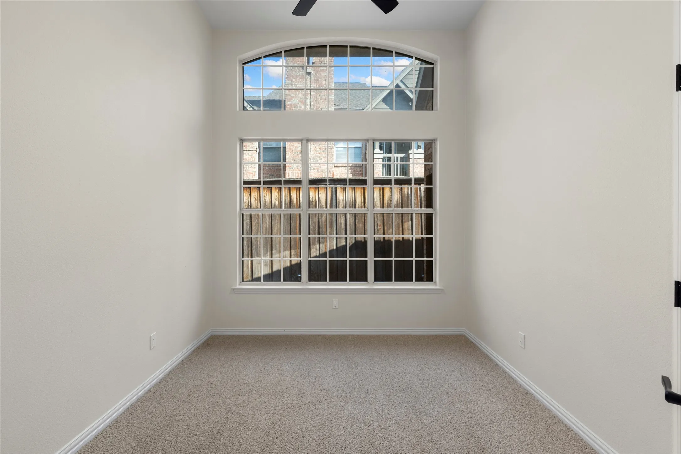 Arched transom window above a multi-pane window, neutral carpet, and a ceiling​​‌​​​​‌​​‌‌​‌‌​​​‌‌​‌​‌​‌​​​‌​​ fan
