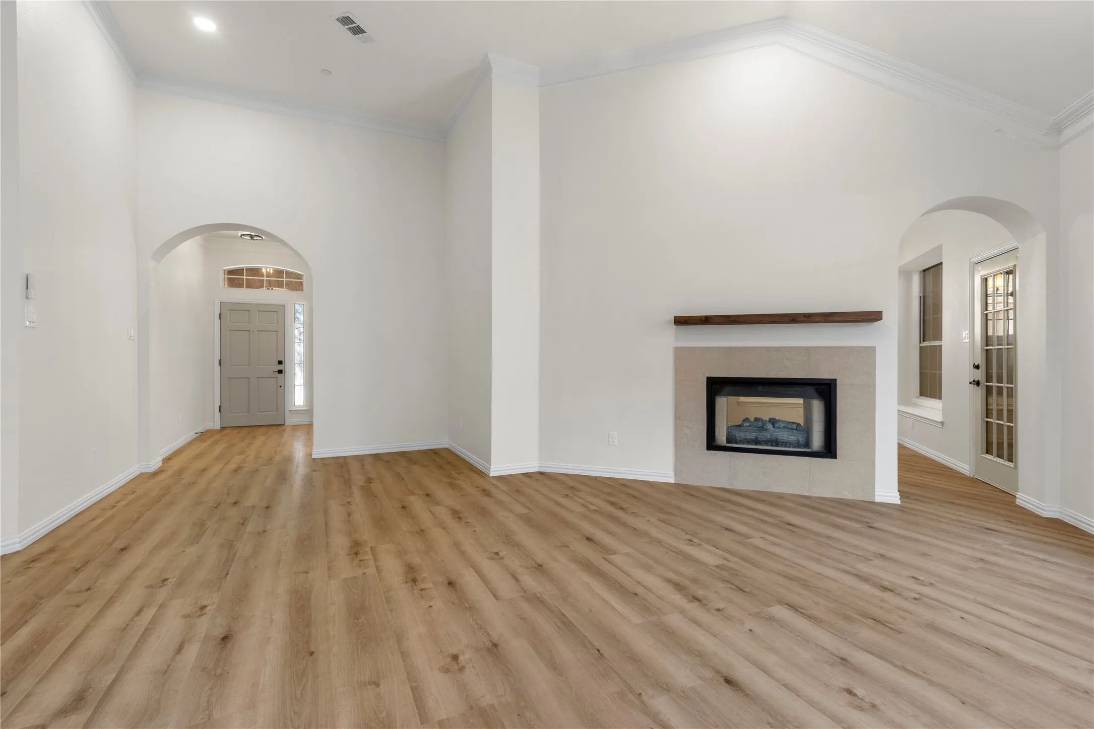 Vaulted ceilings with crown molding, wood-finish flooring, a fireplace with a stone surround, and an arched entry