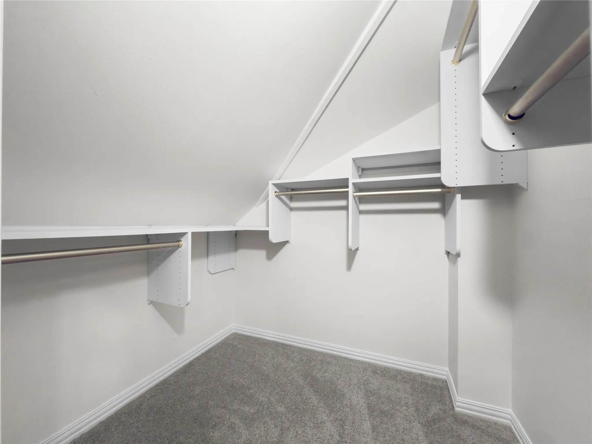 Built-in closet shelving, multiple hanging rods, and sloped ceiling