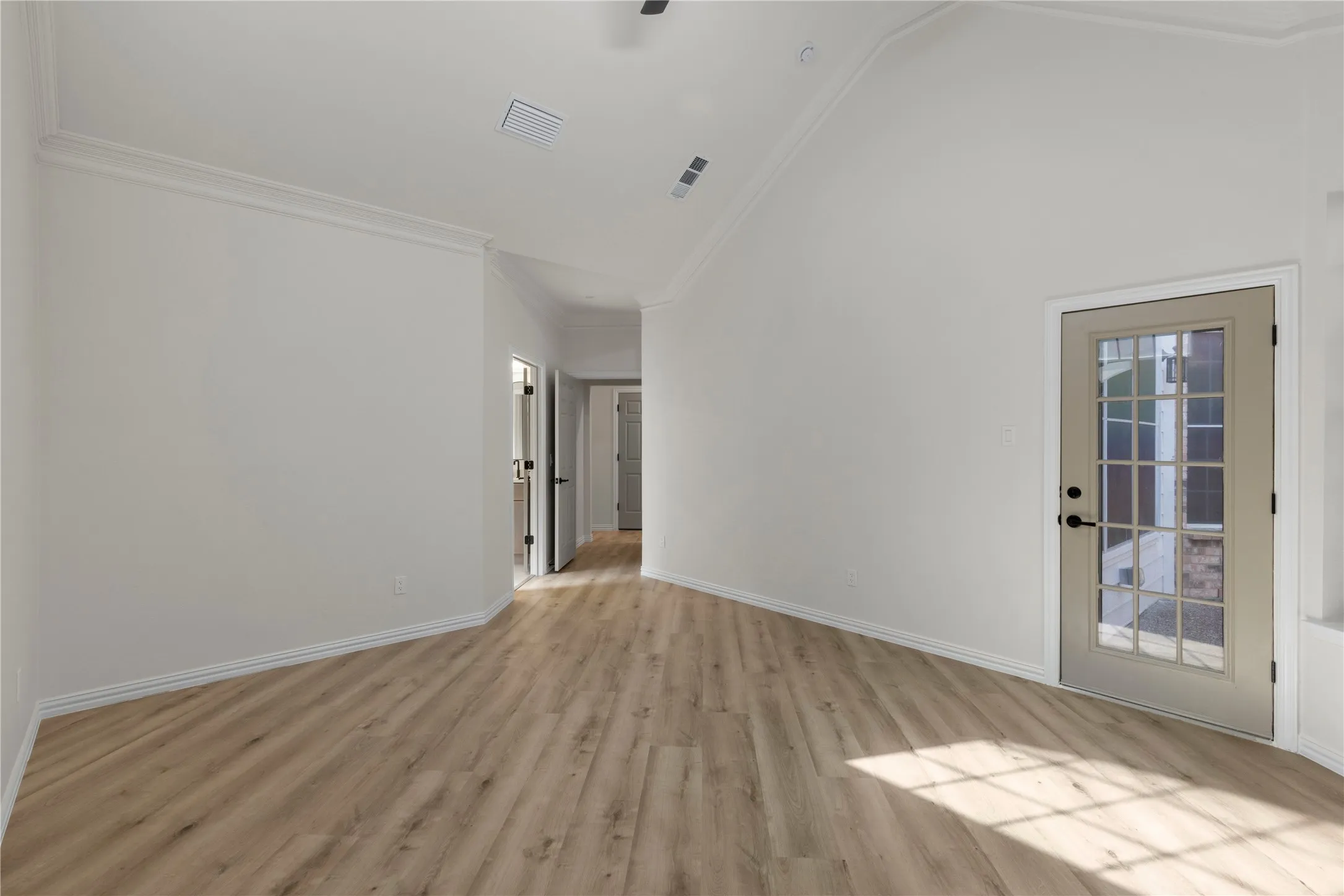 Vaulted ceiling, crown molding, wood-finish flooring, white walls, and a glass-panel door