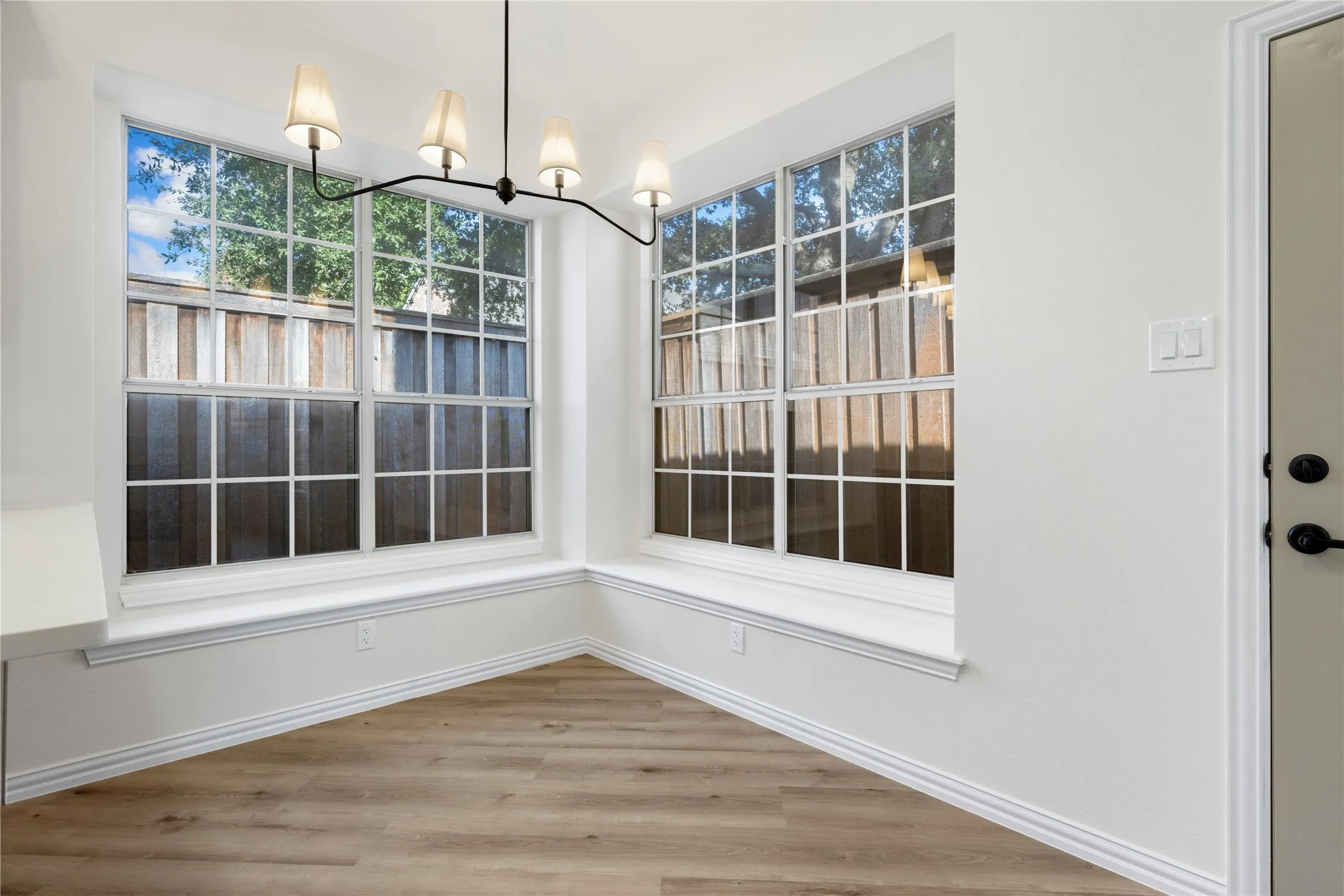 Corner windows with grid panes, wood-finish flooring, and a modern four-light chandelier