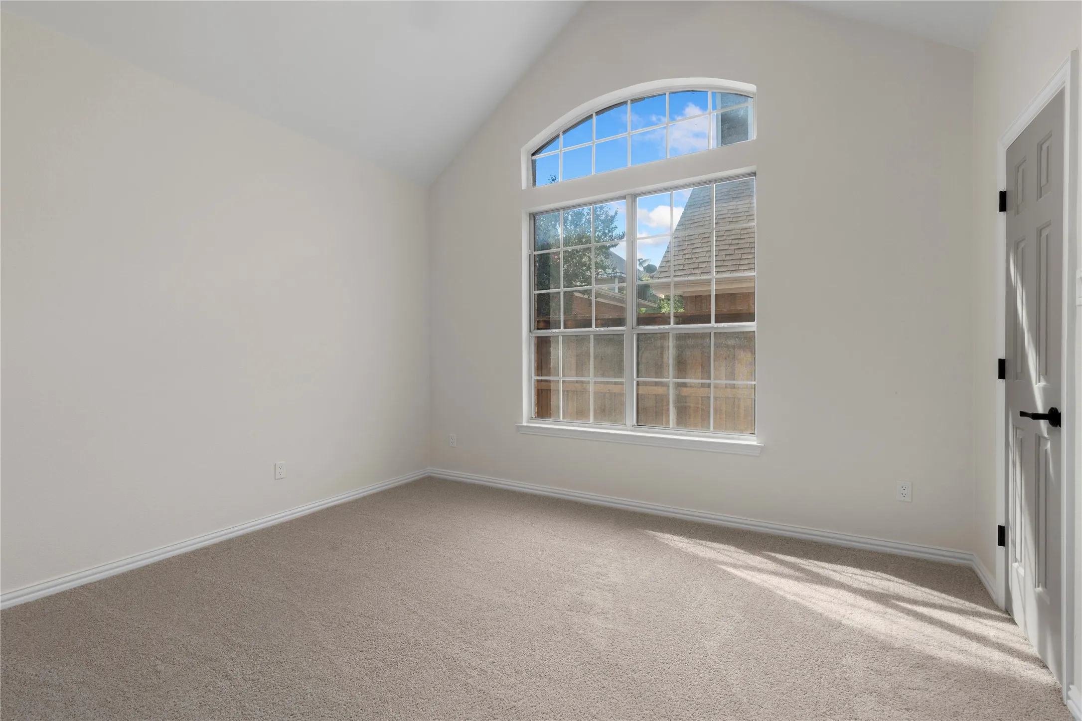 Vaulted ceiling room featuring light-toned carpeting and an arched transom window