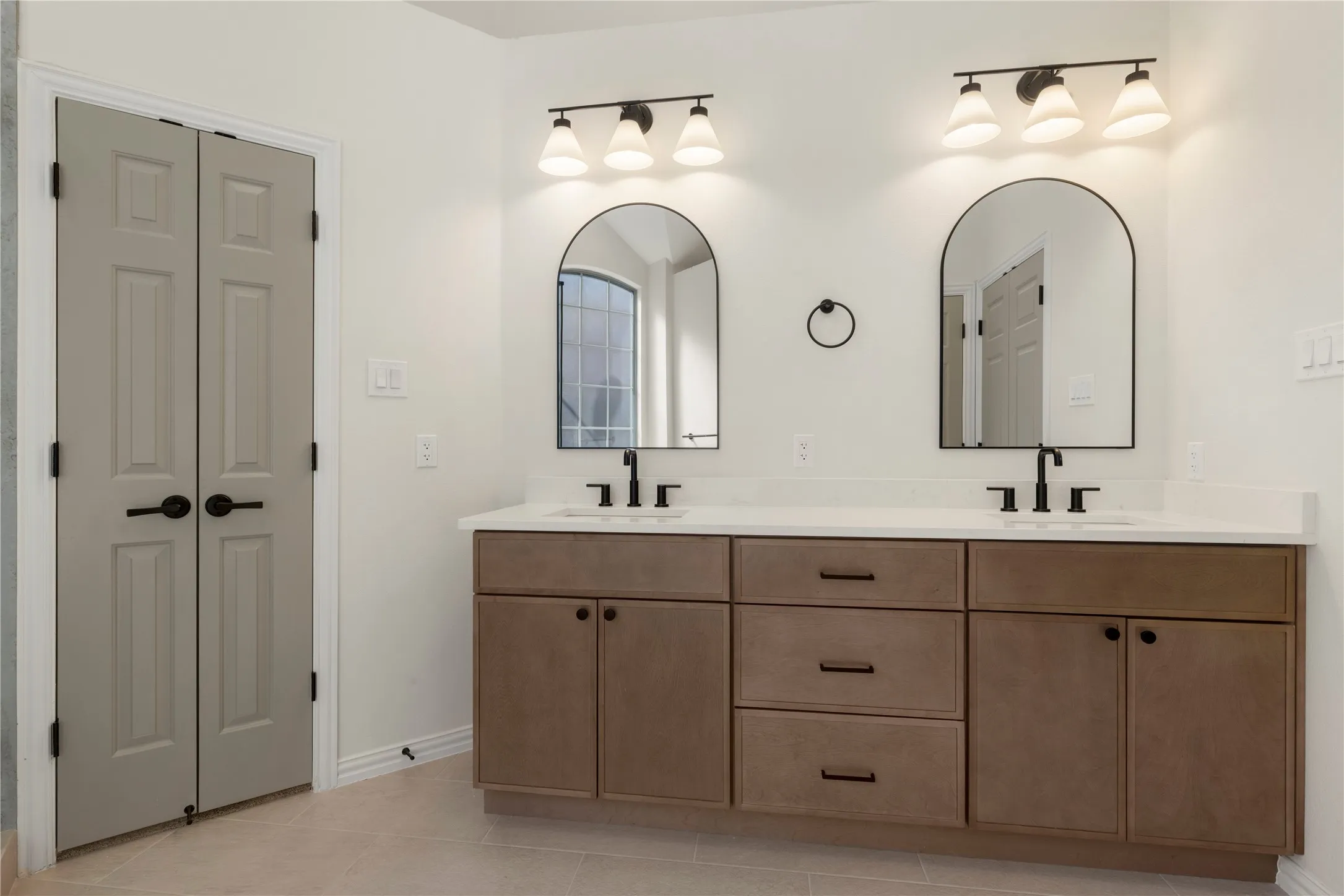 Dual sink vanity with white countertop, arched mirrors, and matte black fixtures