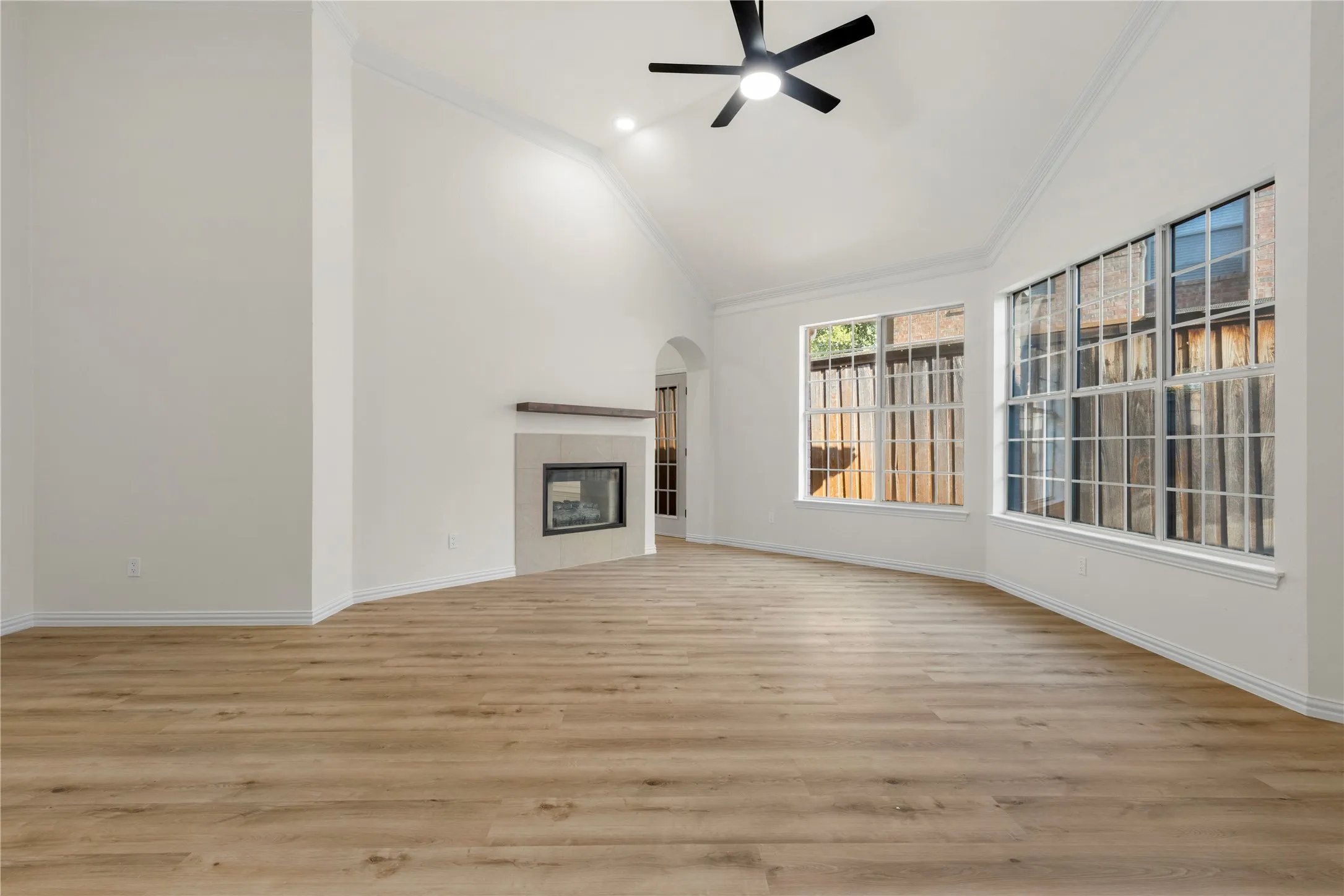 Vaulted ceiling with a ceiling fan, fireplace with a wood mantel, wood-finish flooring, and multiple large windows