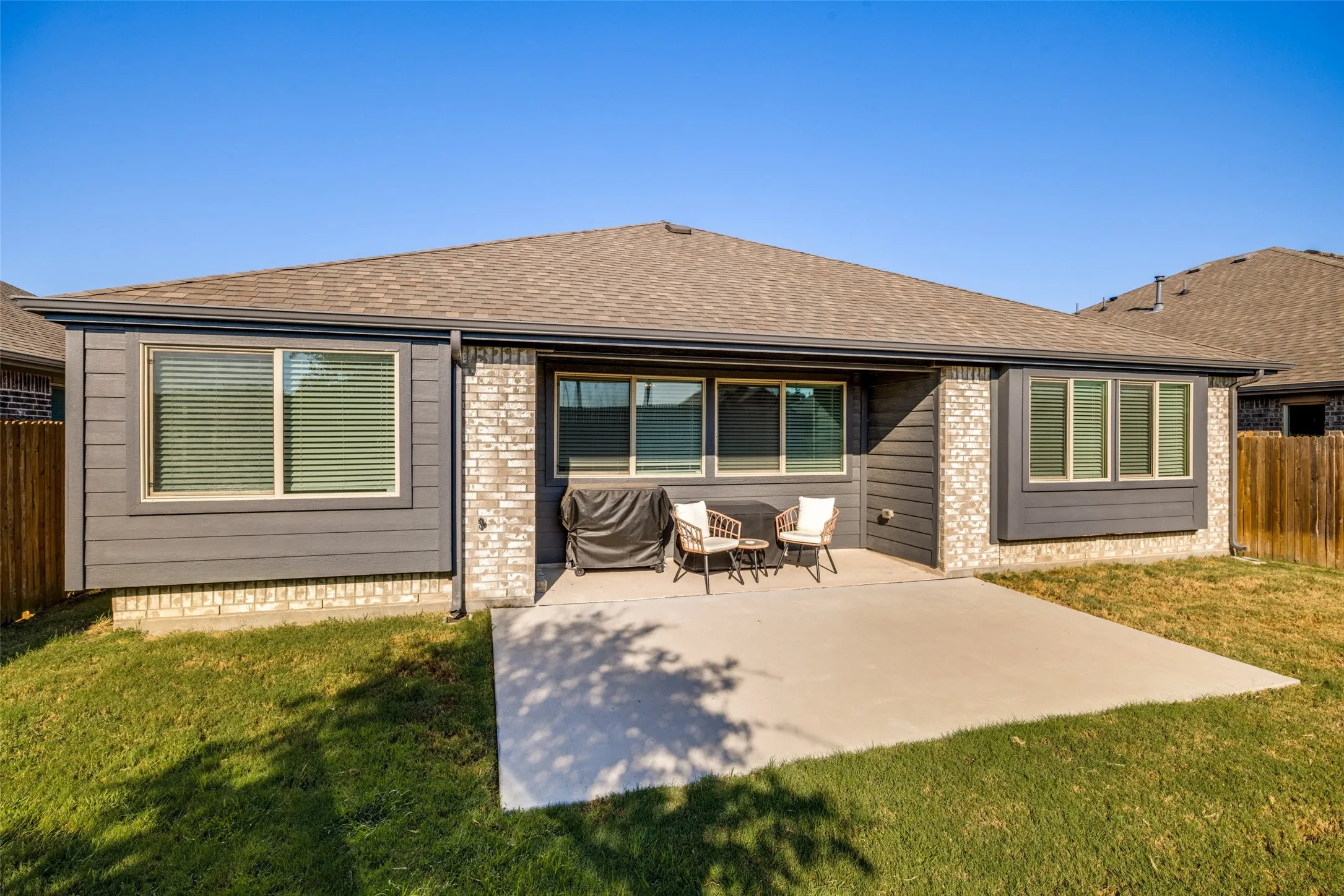 Rear exterior with a concrete patio, gray horizontal siding, light-toned brick accents, and multiple windows