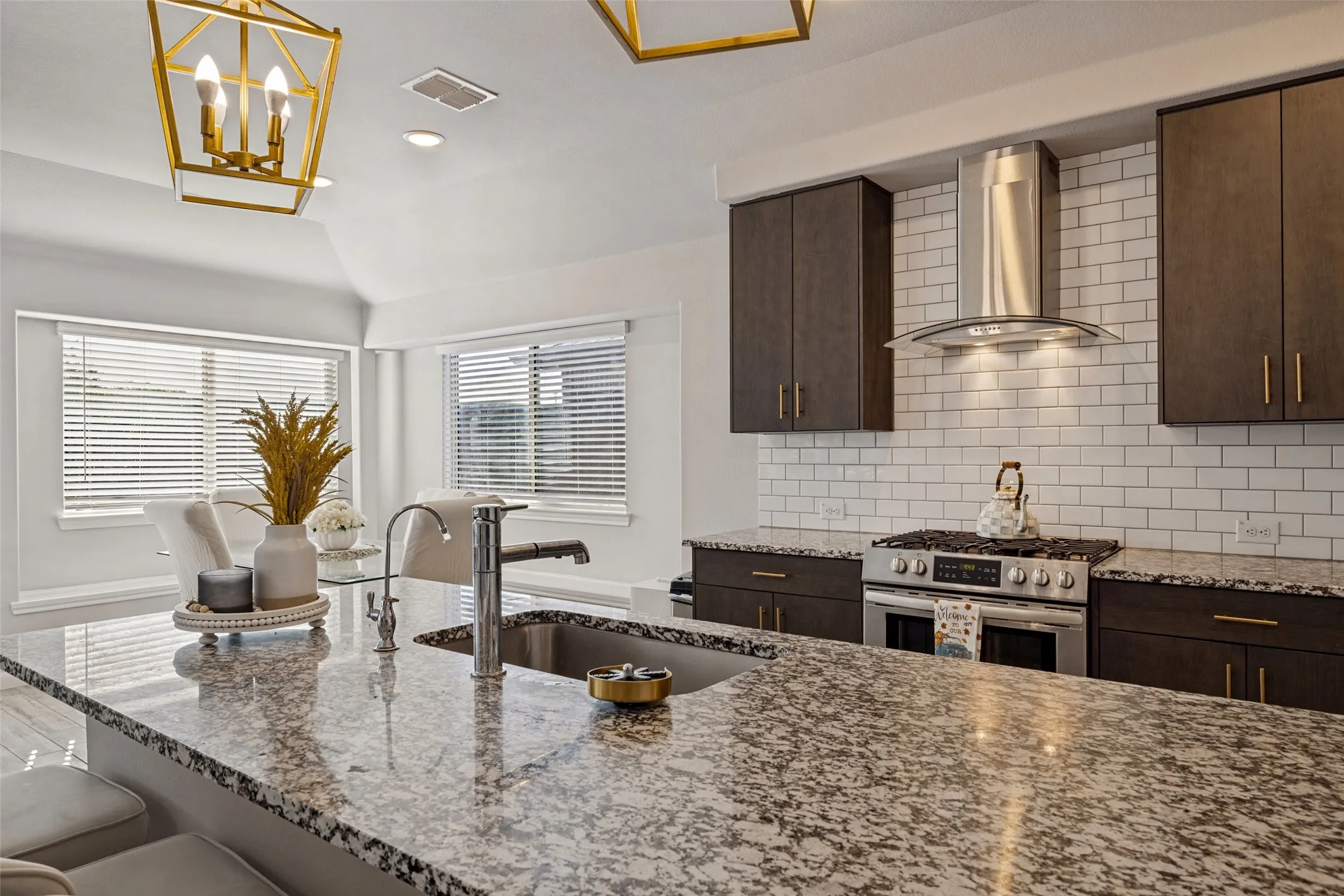 Spacious kitchen featuring expansive granite countertops, dark wood cabinetry, a stainless steel range with a ventilation hood, subway tile backsplash, and recessed lighting