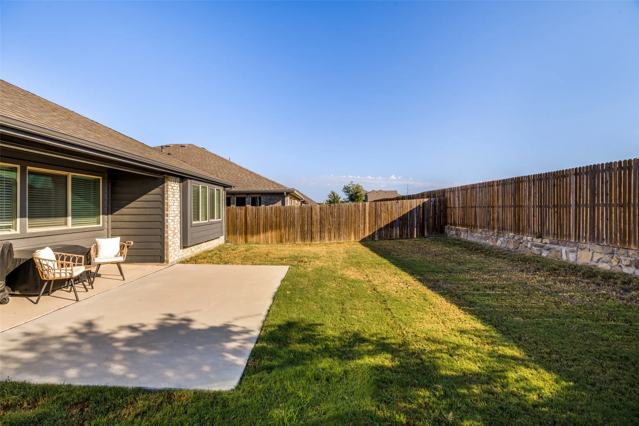 Expansive backyard featuring a concrete patio, a full privacy fence, and a manicured lawn
