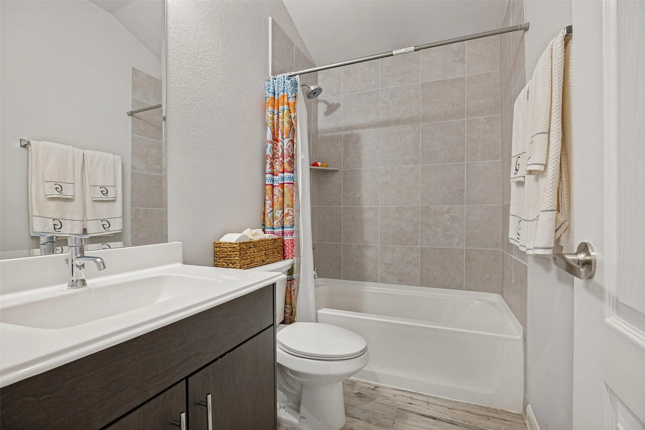 Bathroom featuring a vanity with an integrated sink, dark wood-finish cabinetry, a toilet, and a tiled shower-tub combination