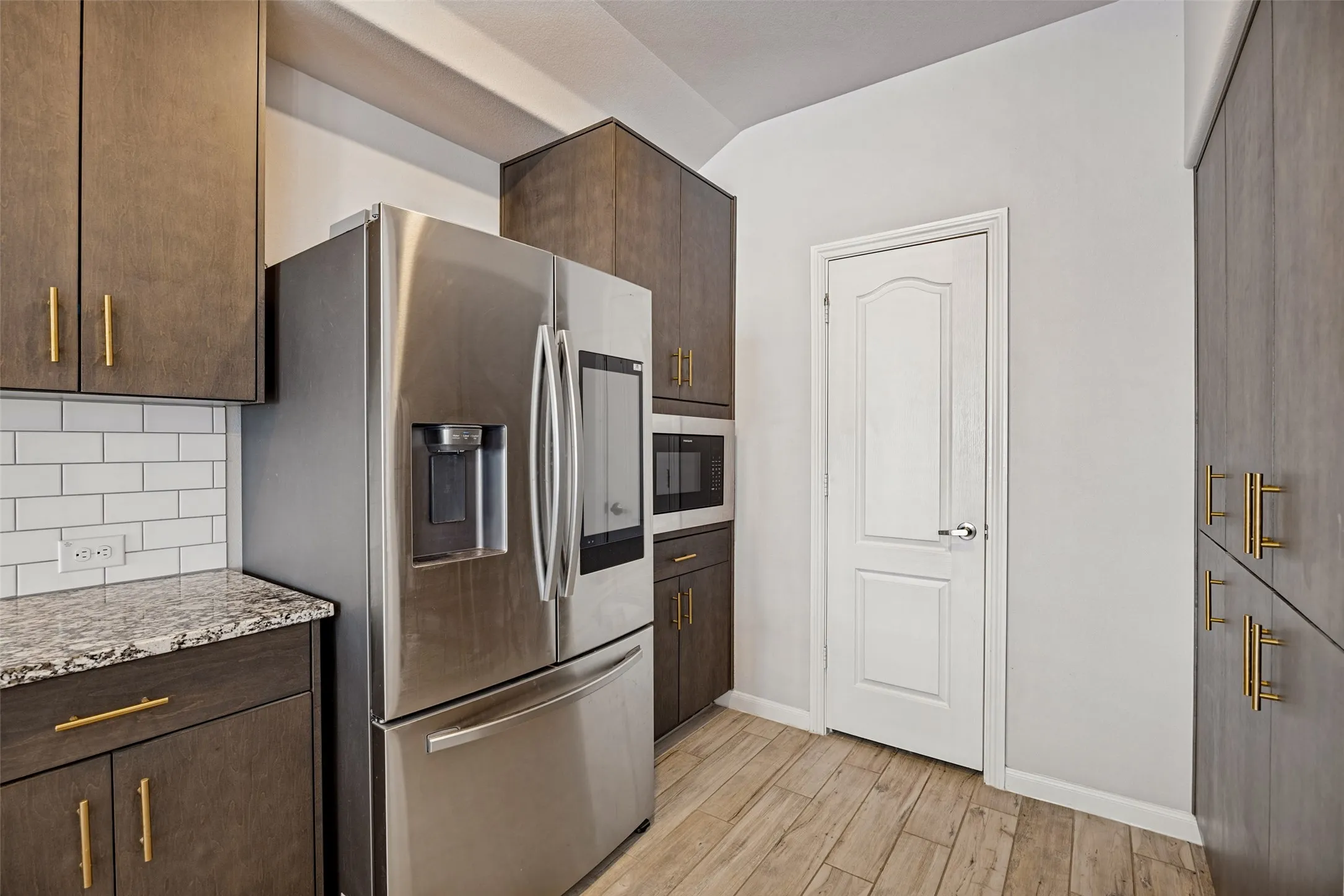 Stainless steel French door refrigerator, built-in microwave, wood-finish flooring, white subway tile backsplash, and granite-look countertops