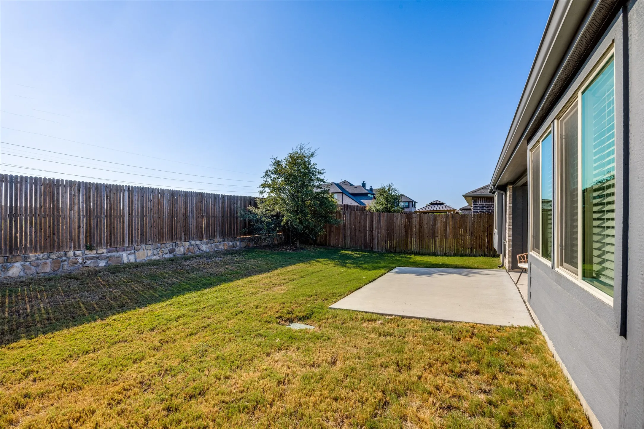 Expansive backyard featuring a wood privacy fence with stone detailing, a concrete patio, and mature landscaping