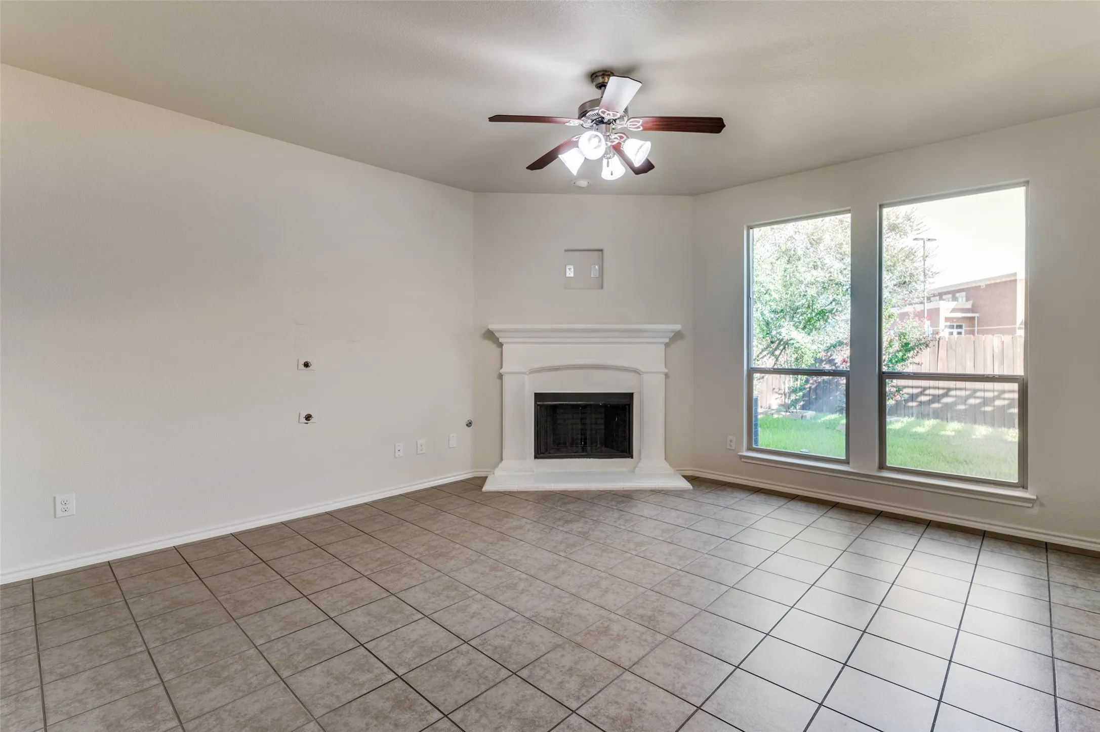 Unfurnished living room featuring a ceiling fan, light tile patterned flooring, and a fireplace with raised hearth