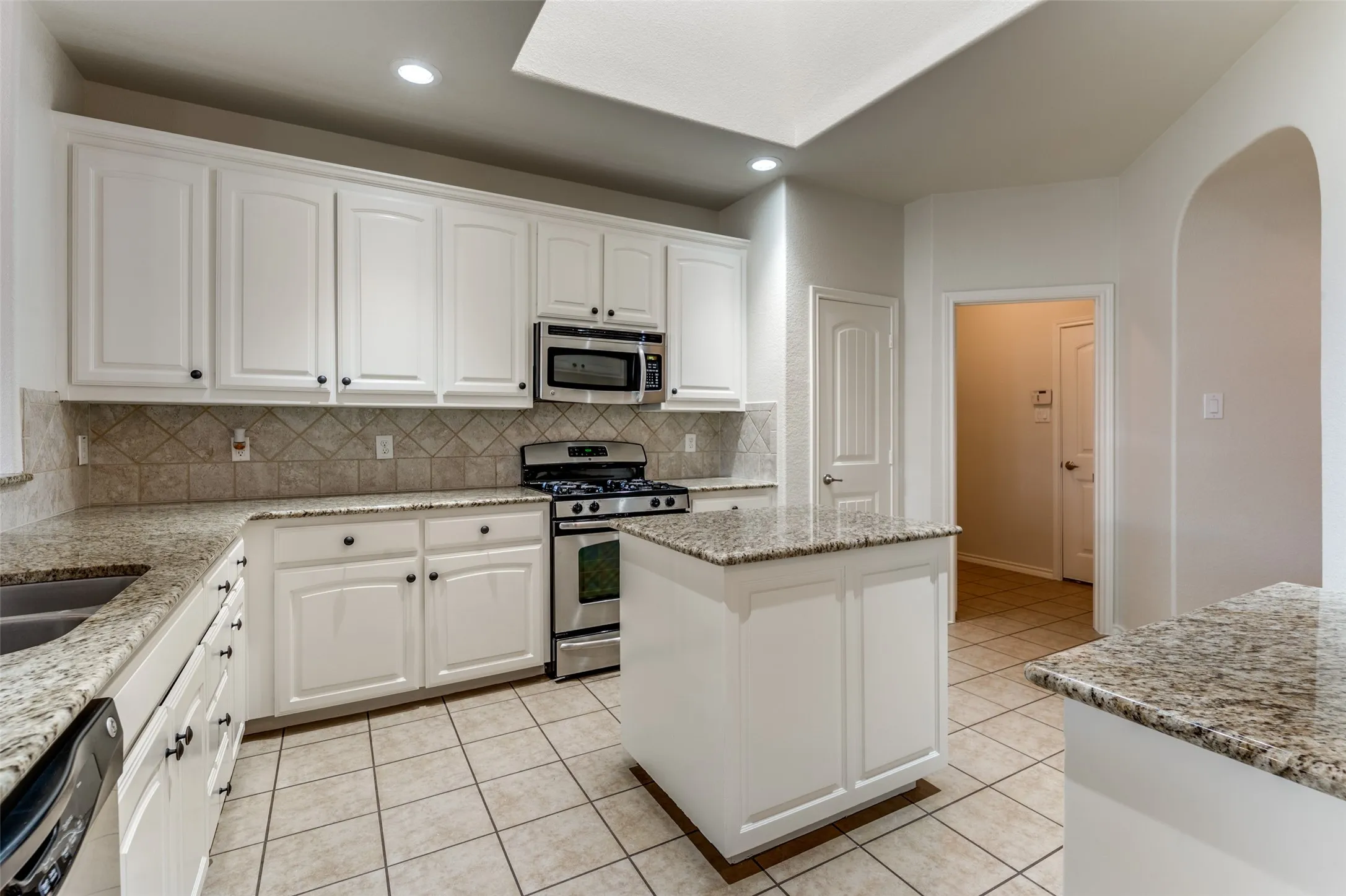 Kitchen with appliances with stainless steel finishes, arched walkways, light tile patterned floors, white cabinetry, and recessed lighting