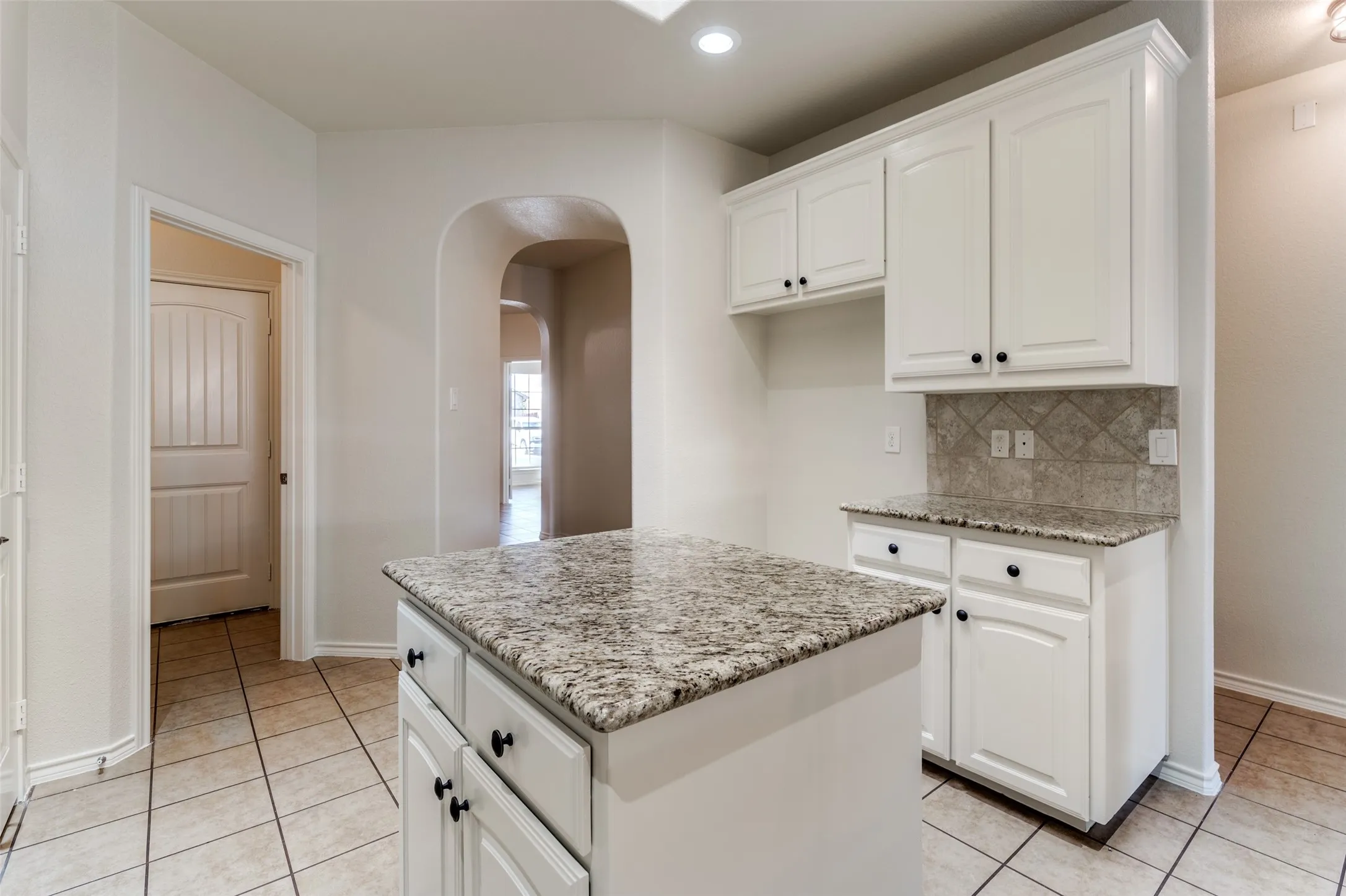 Kitchen with a kitchen island, arched walkways, light stone counters, light tile patterned floors, and white cabinetry