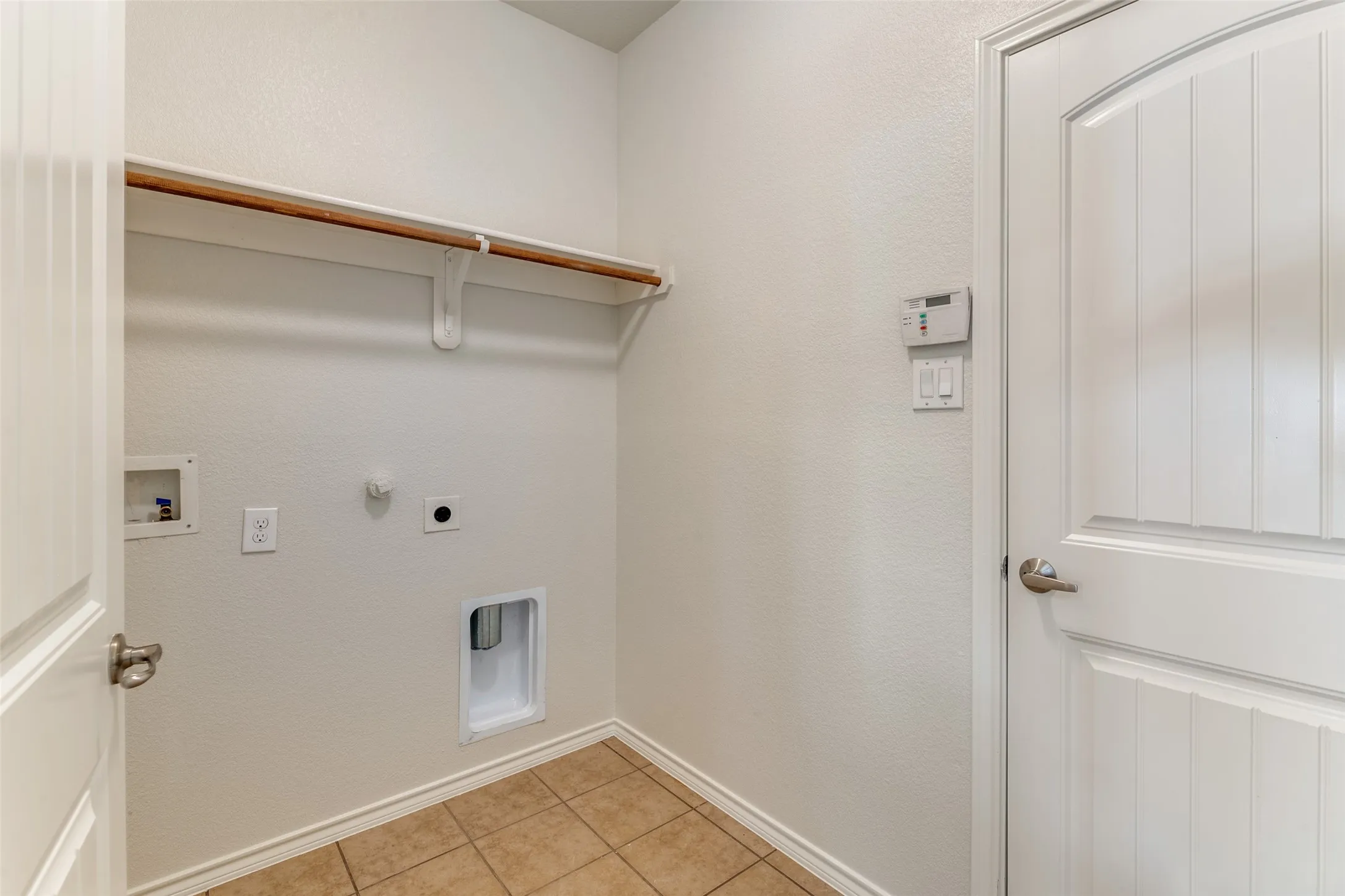 Washroom with hookup for a washing machine, hookup for an electric dryer, hookup for a gas dryer, light tile patterned flooring, and a textured wall