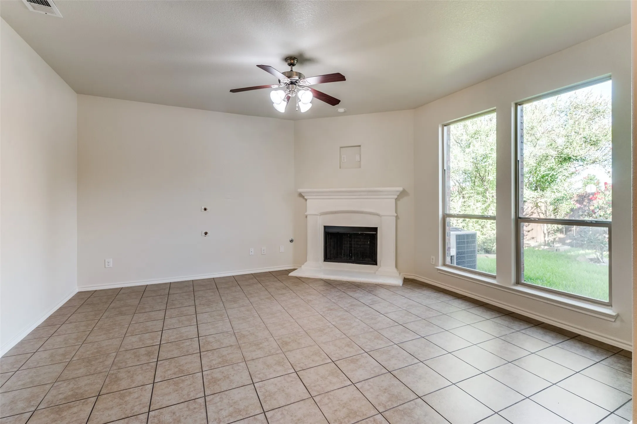 Unfurnished living room with ceiling fan, a fireplace with raised hearth, and light tile patterned floors