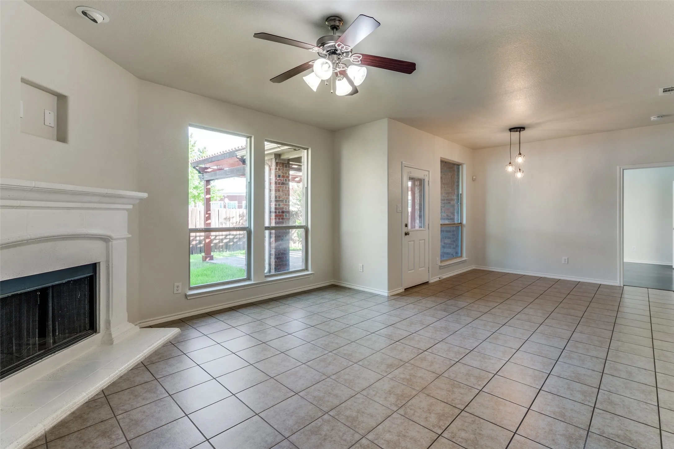 Unfurnished living room with light tile patterned floors, a ceiling fan, and a fireplace with raised hearth