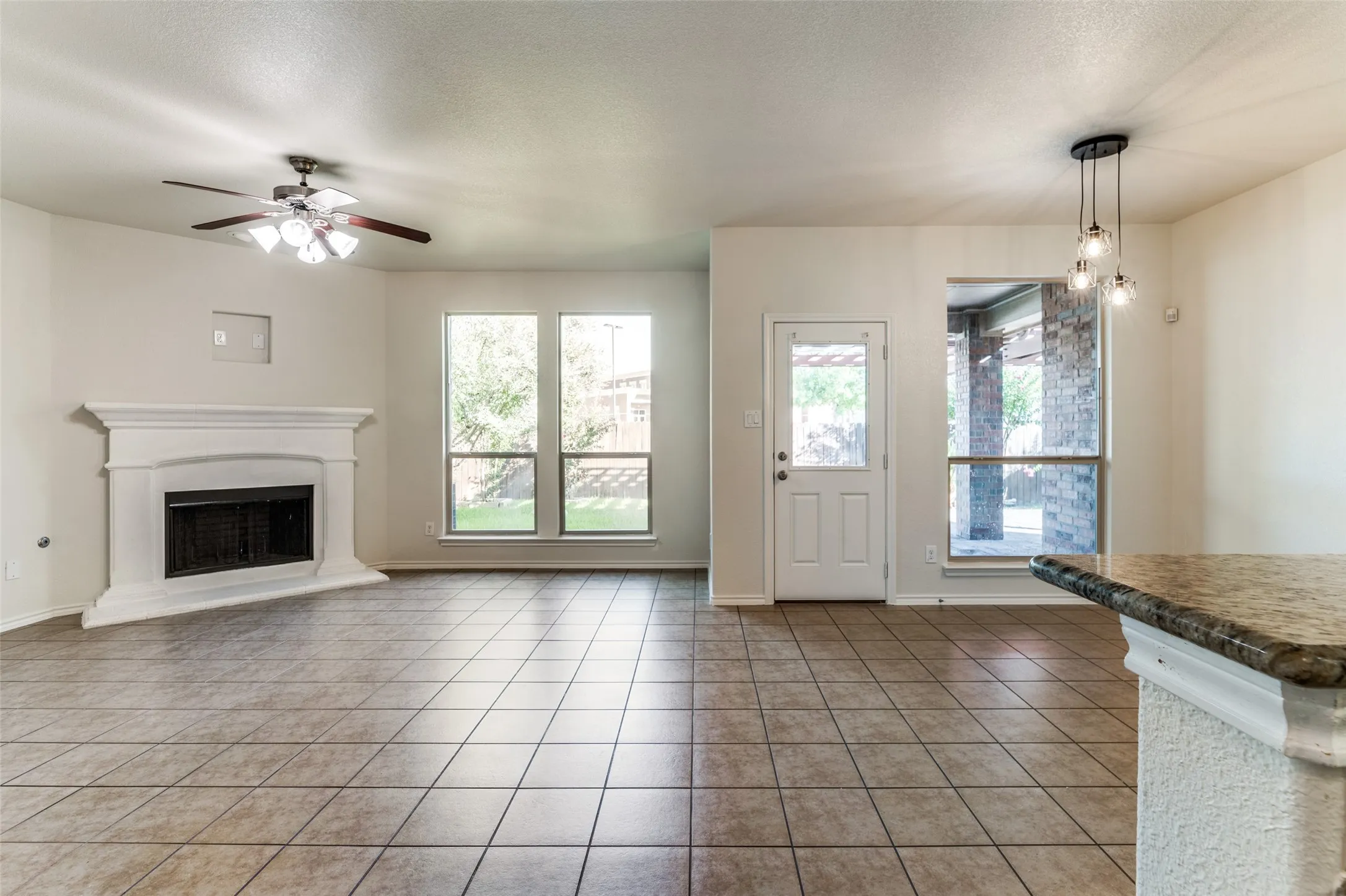 Unfurnished living room featuring a textured ceiling, plenty of natural light, light tile patterned floors, a fireplace with raised hearth, and ceiling fan