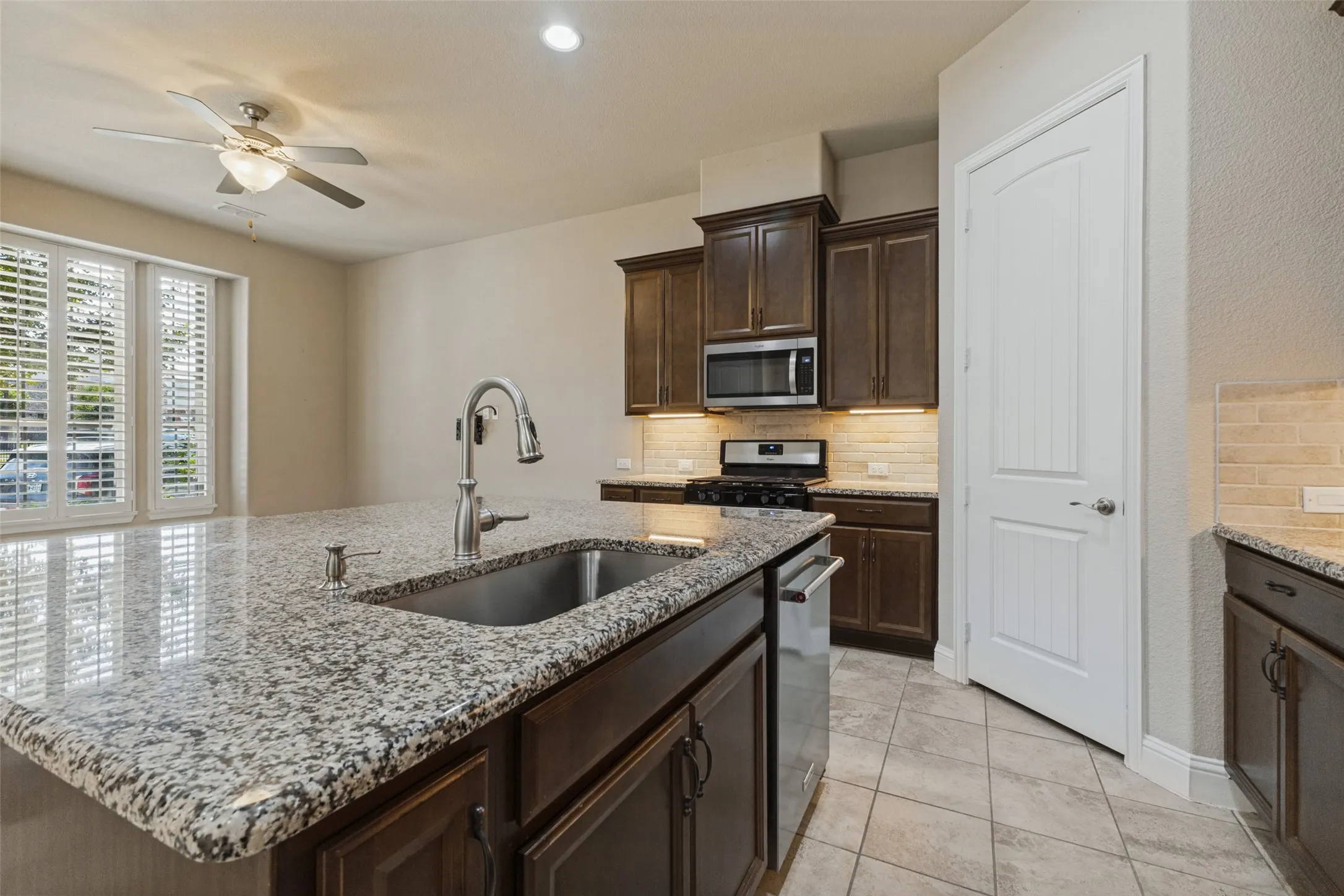 Kitchen island with granite countertop and undermount sink, stainless steel appliances with gas cooktop range, and walk-in pantry