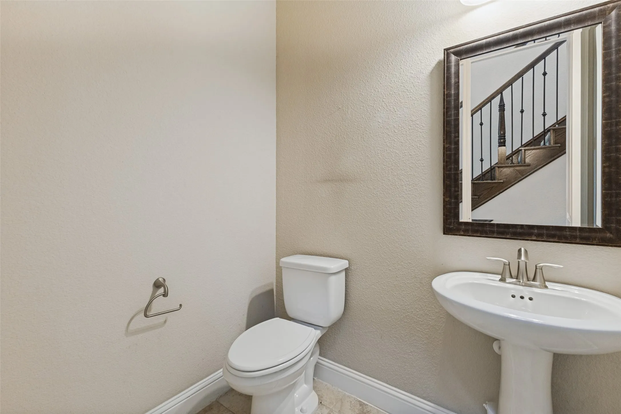 Downstairs guest powder bath with pedestal sink with brushed nickel features and framed mirror